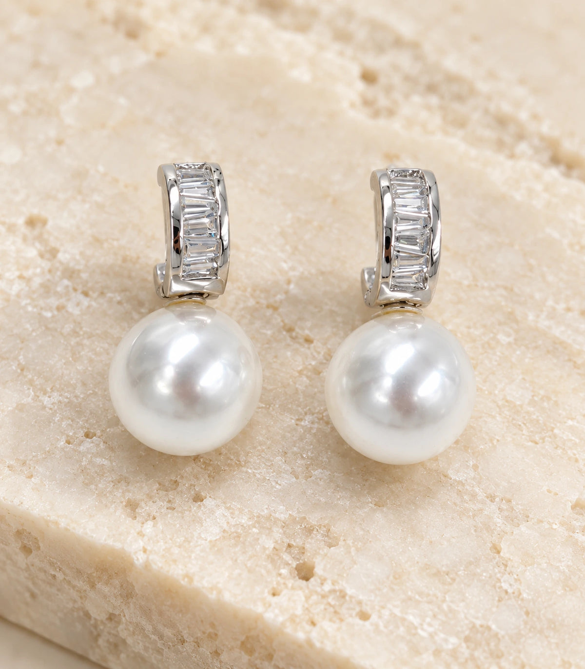 Close view of the silver baguette huggie earring pair with white pearl-style drops on stone
