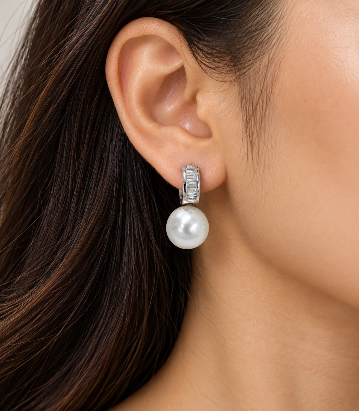 Silver baguette huggie earring with a white pearl-style drop in an editorial worn view