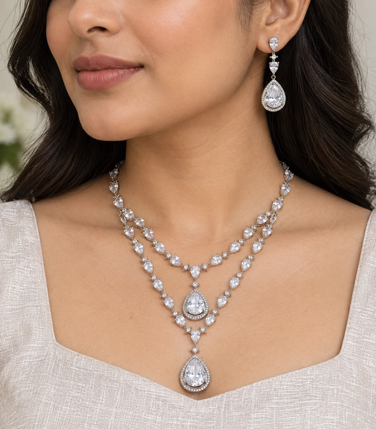 Closeup of layered teardrop necklace and matching earring worn with an ivory outfit