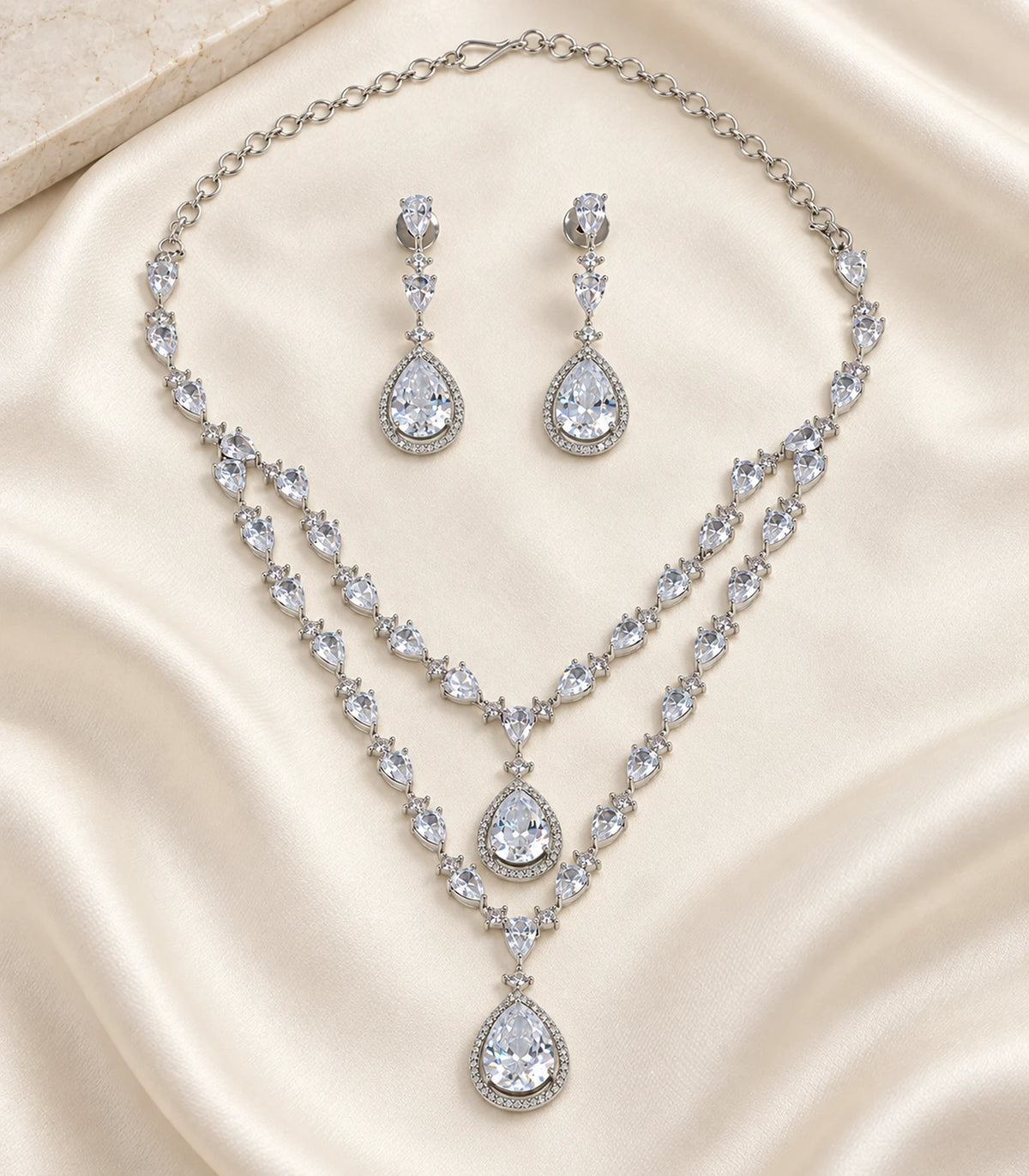 Complete silver clear layered teardrop necklace and earring pair arranged on pale fabric