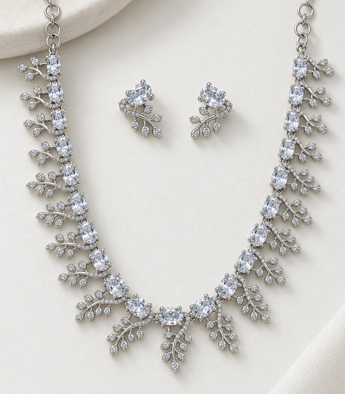 Clear oval stones and branching leaf details on the necklace and matching earrings on fabric