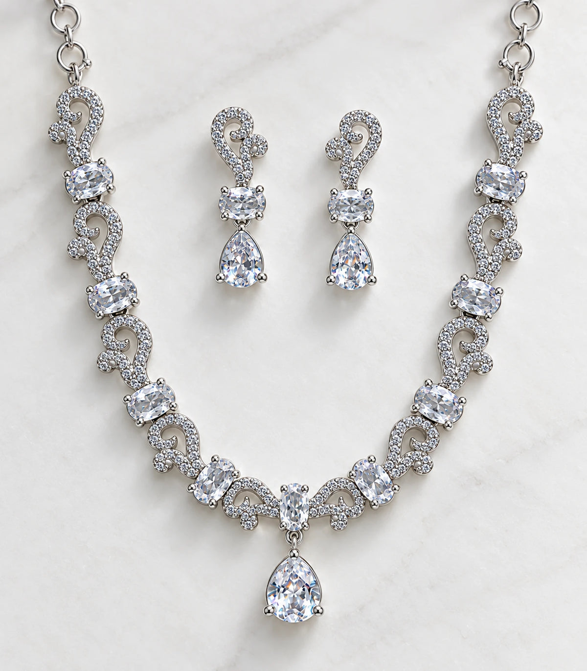 Detail of the silver-tone paisley necklace and matching clear teardrop drop earrings on a pale surface