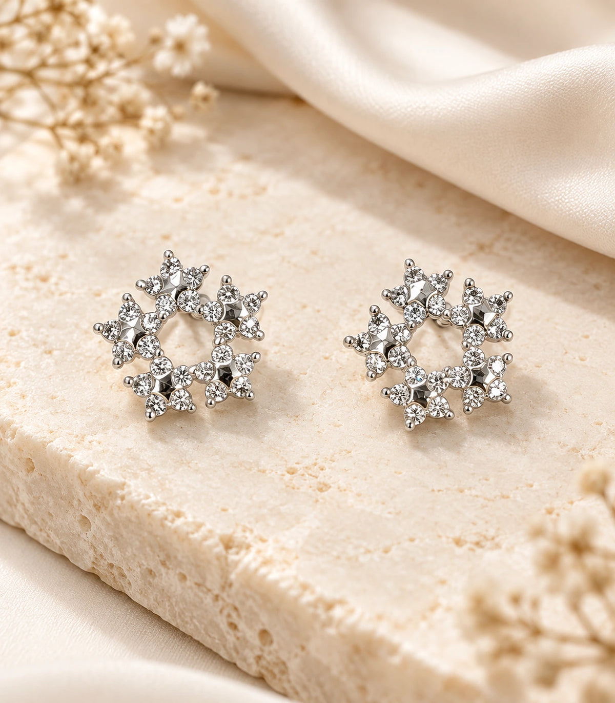 Matching pair of silver-tone butterfly wreath stud earrings styled on a pale textured surface