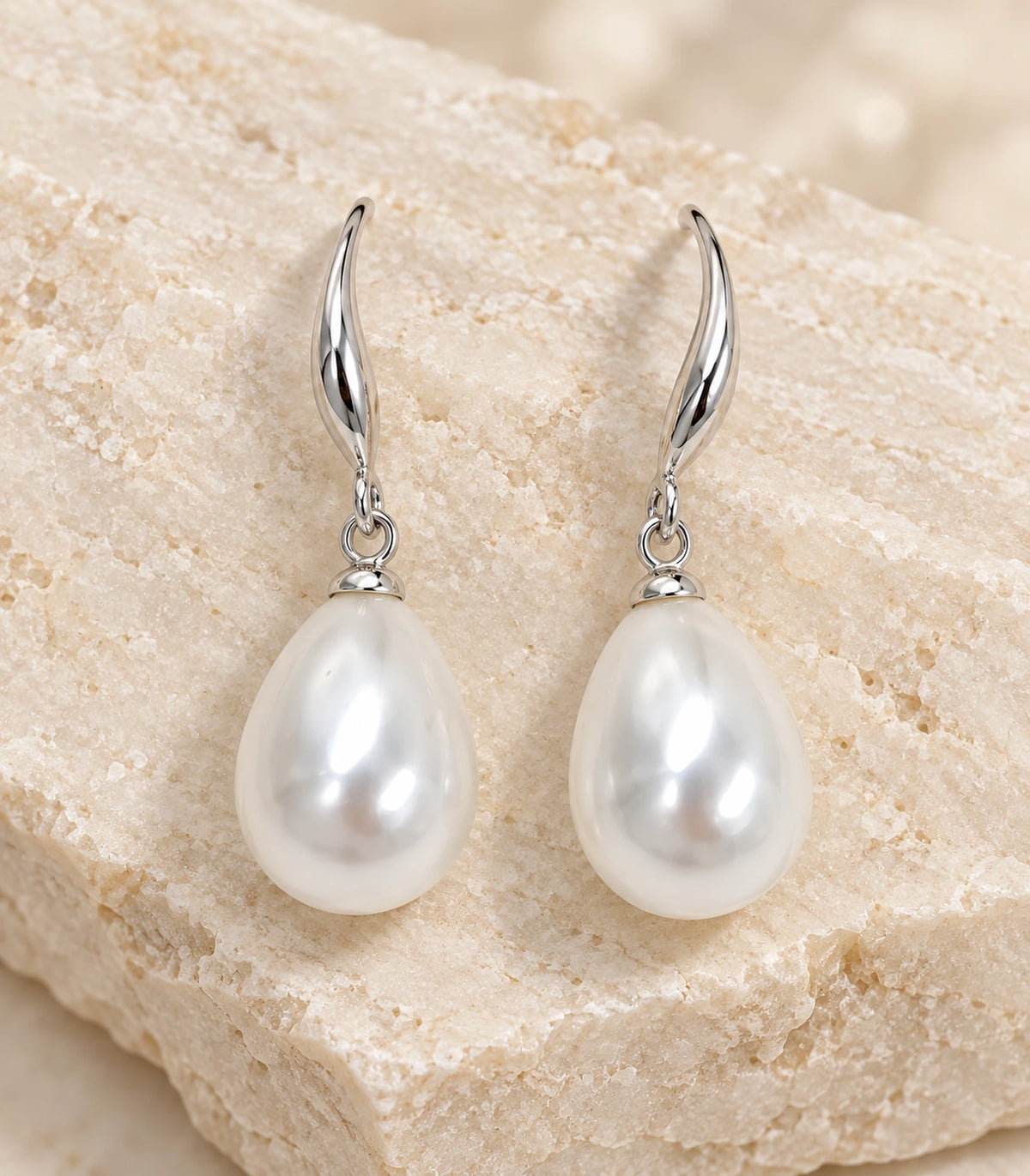 Close detail of the pair of silver-tone curved leaf earrings and white teardrop pearl-style drops on stone