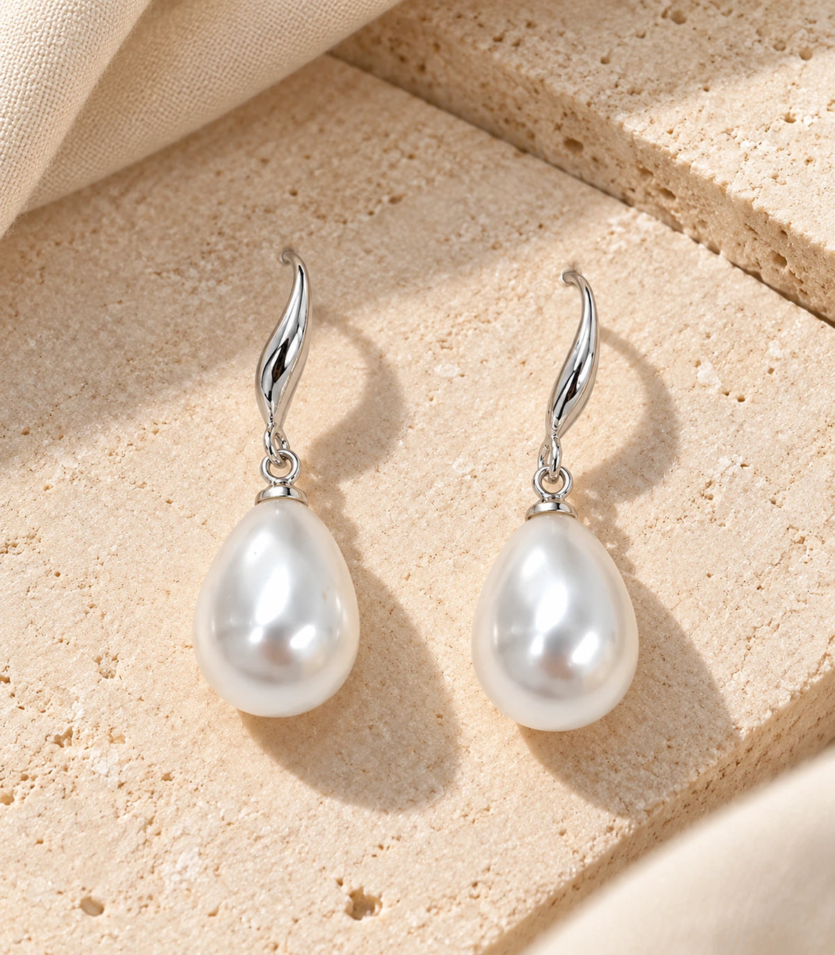 Pair of silver-tone curved leaf teardrop pearl-style earrings arranged on a stone surface