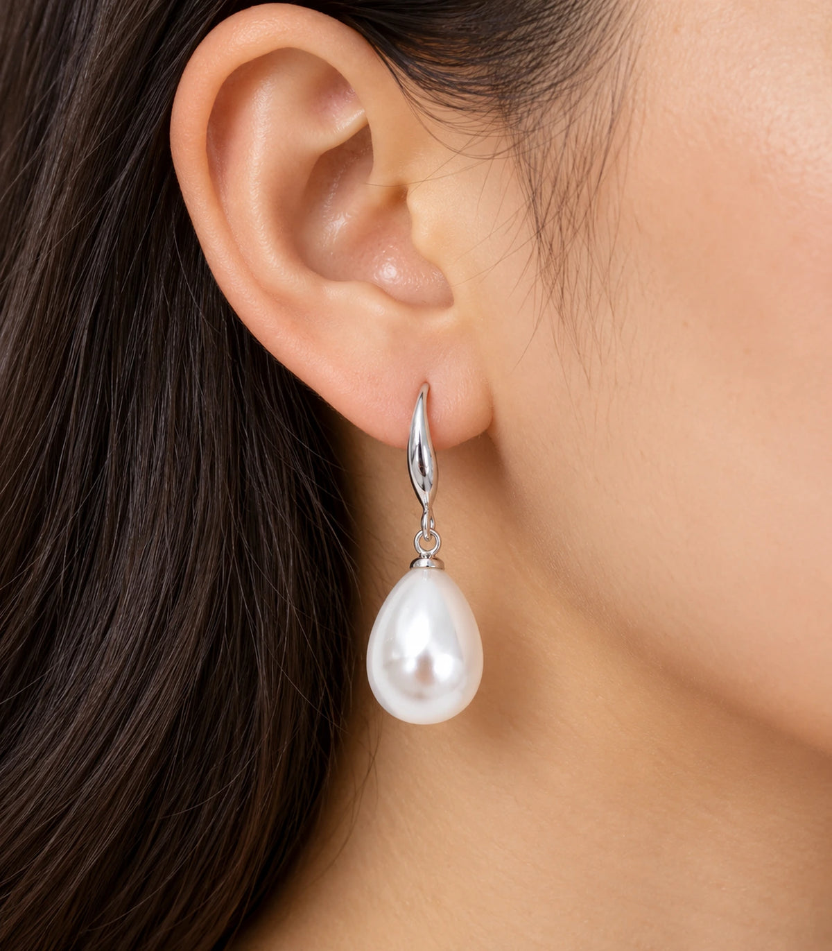 Silver-tone curved leaf earring with a white teardrop pearl-style drop worn on one ear