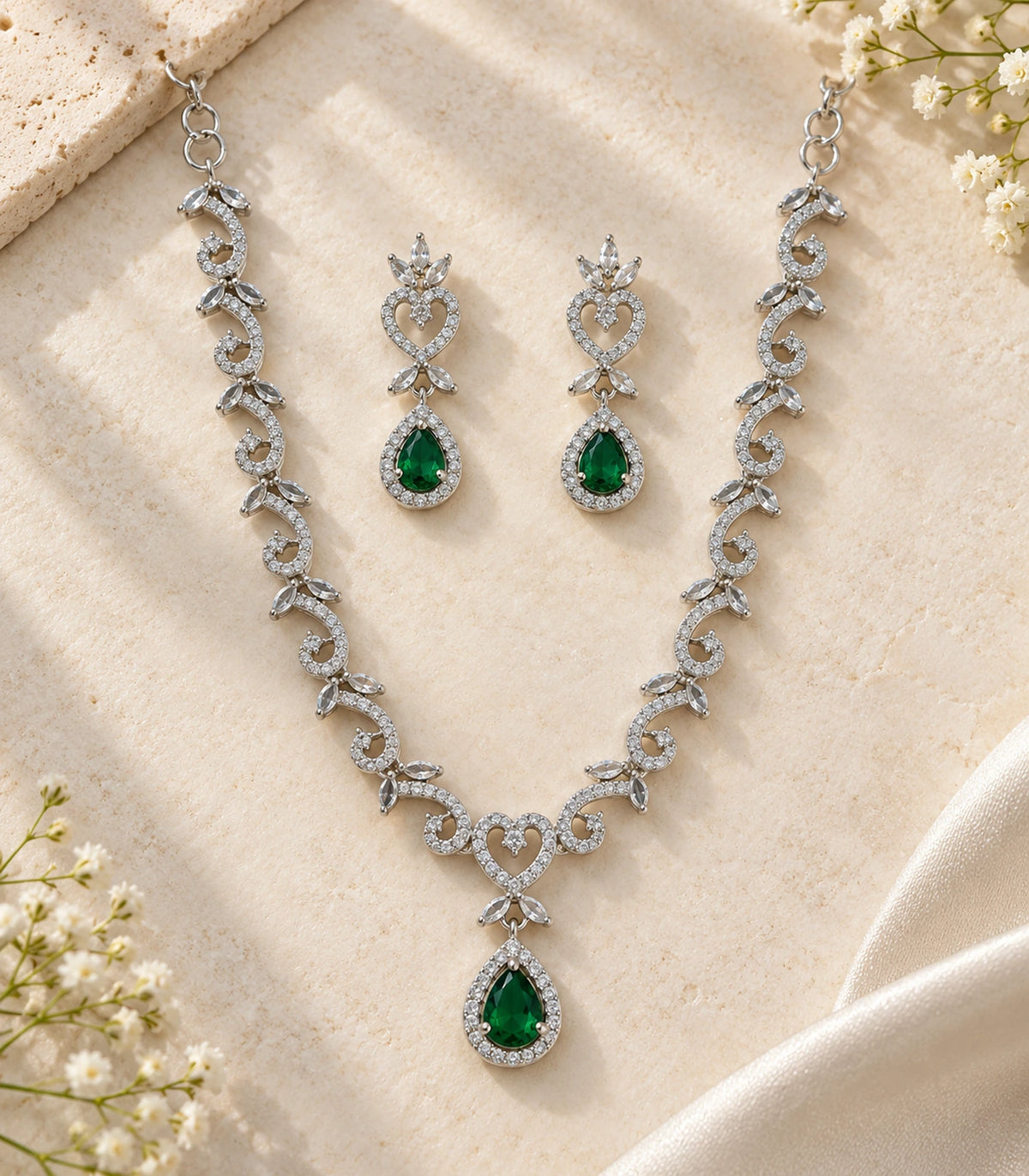 Silver-tone scroll and heart necklace with matching green drop earrings in a styled flat lay