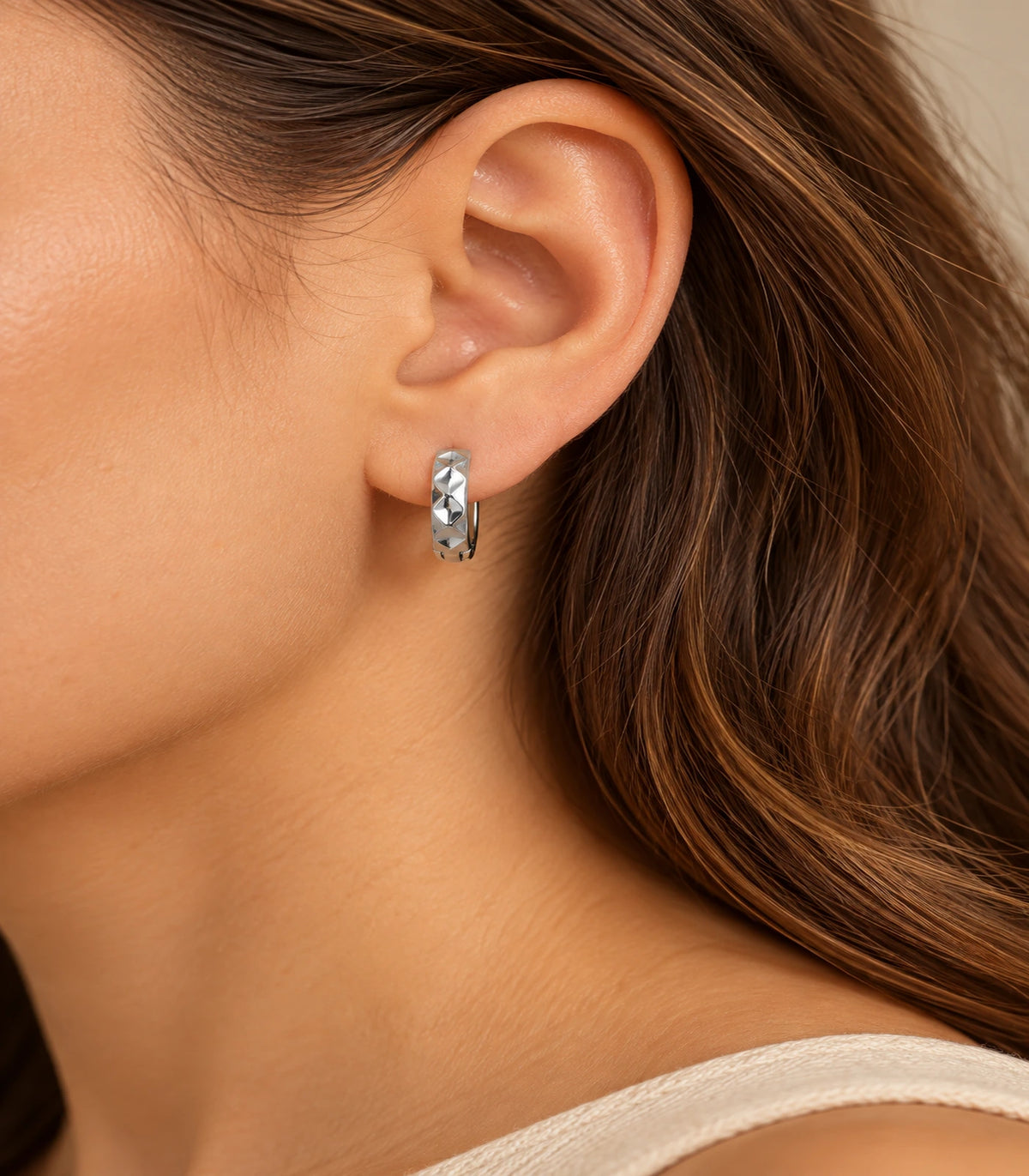 JIMIKI silver faceted diamond pattern huggie earrings, worn in warm editorial lighting #color_silver