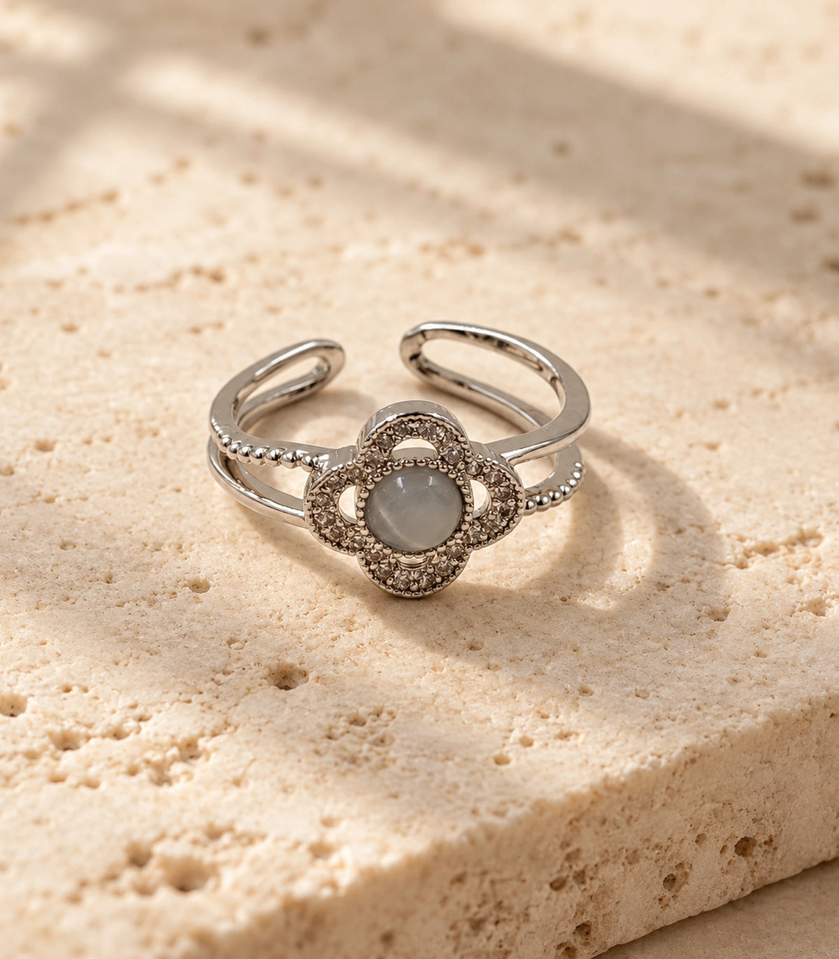 Complete silver-tone grey cabochon clover ring on a stone surface