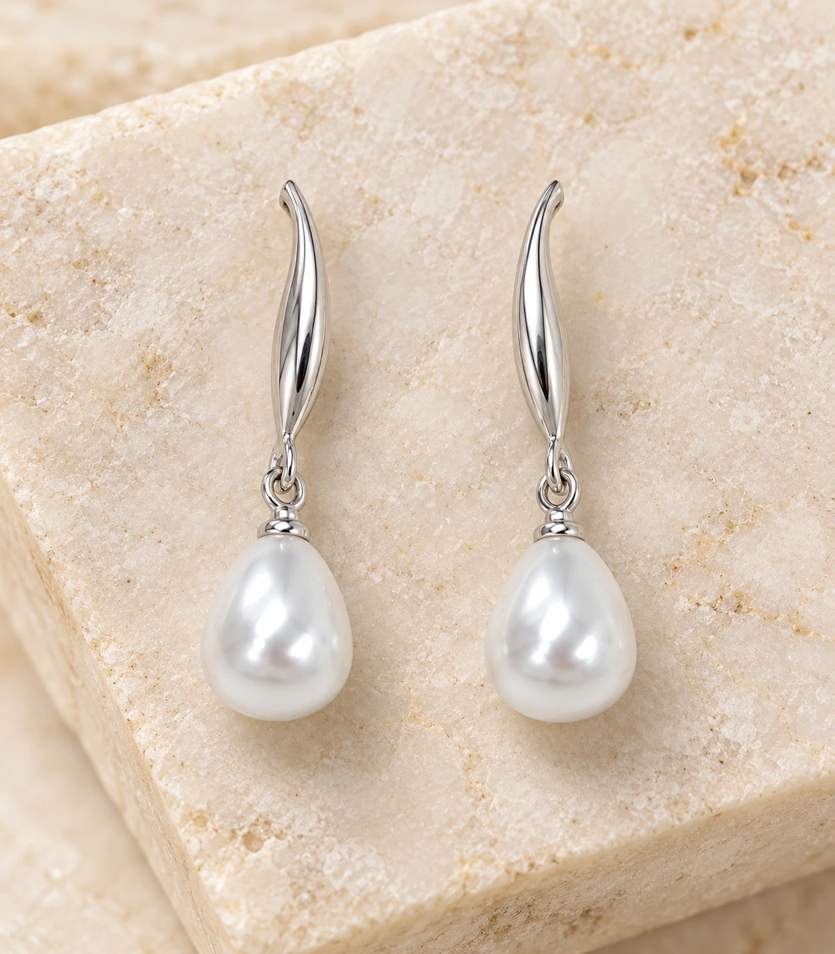 Close view of the matching leaf and teardrop pearl-style earring pair on textured cream stone