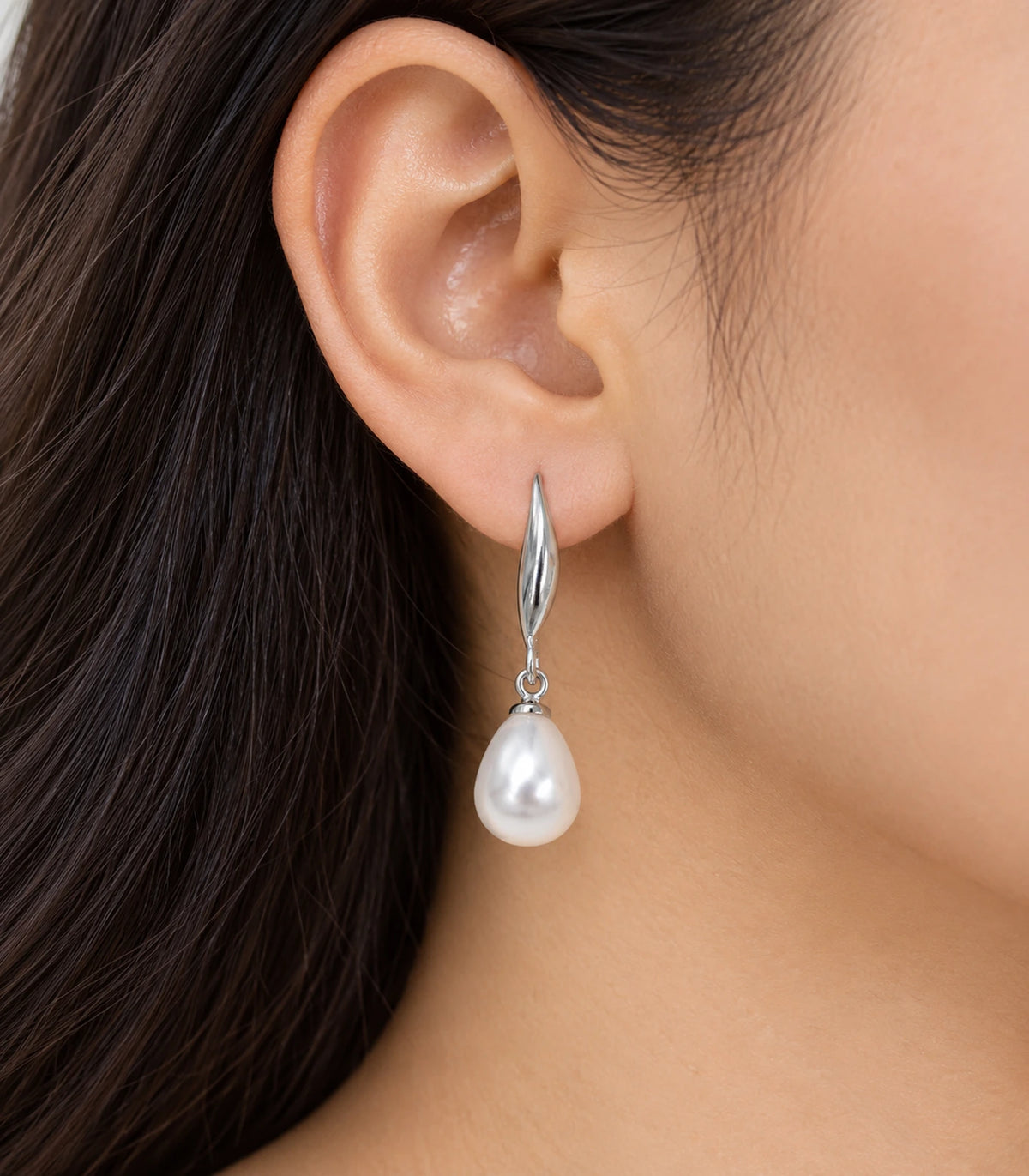 Silver-tone leaf and white teardrop pearl-style earring worn on one ear
