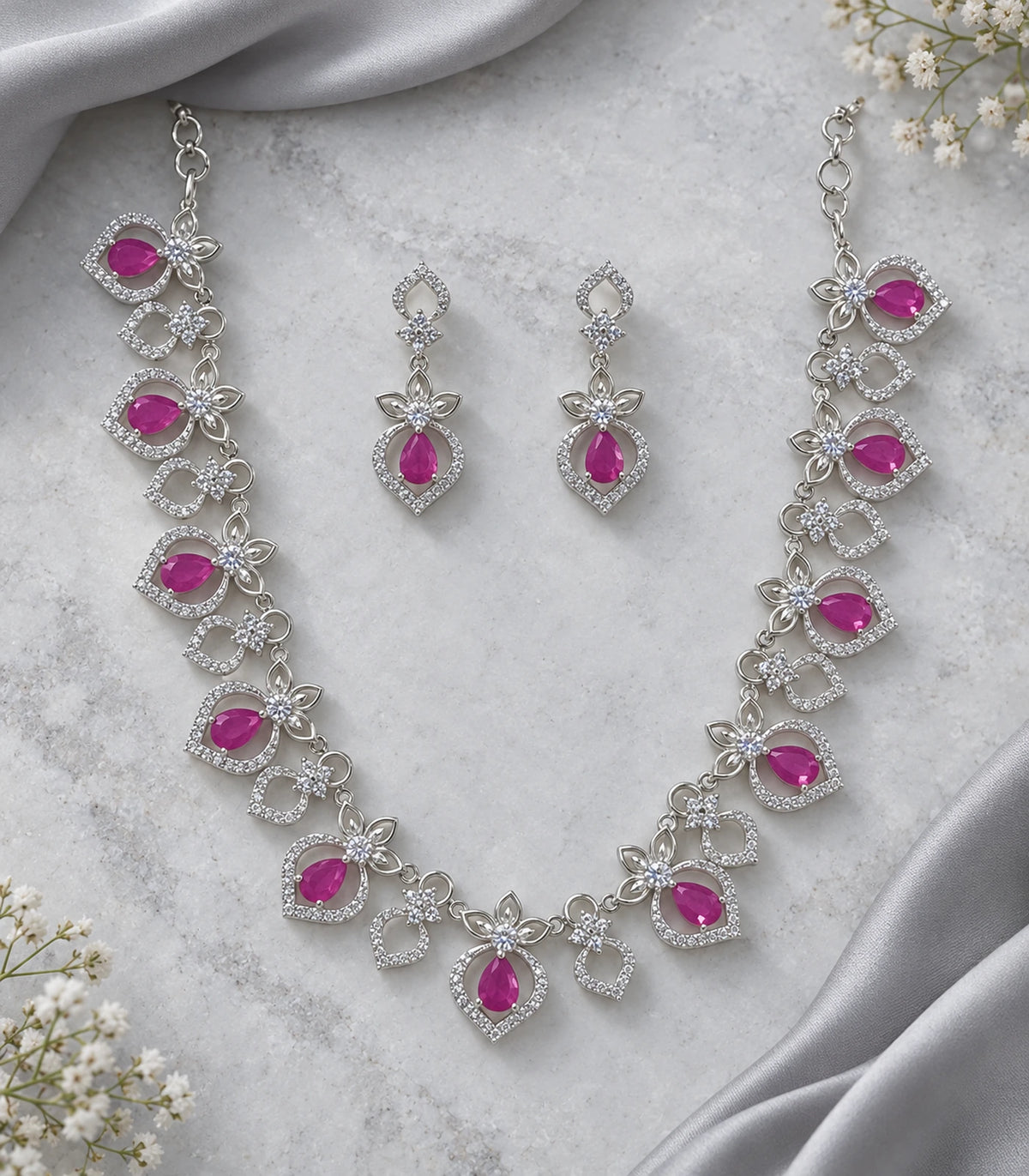 Silver-tone magenta necklace set and matching earring pair on a styled flatlay