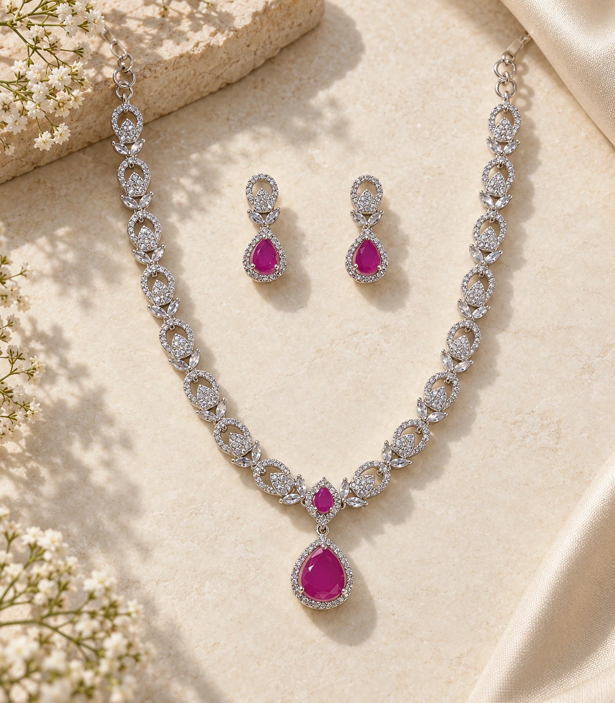 Silver-tone necklace and matching magenta teardrop earrings arranged on a cream surface