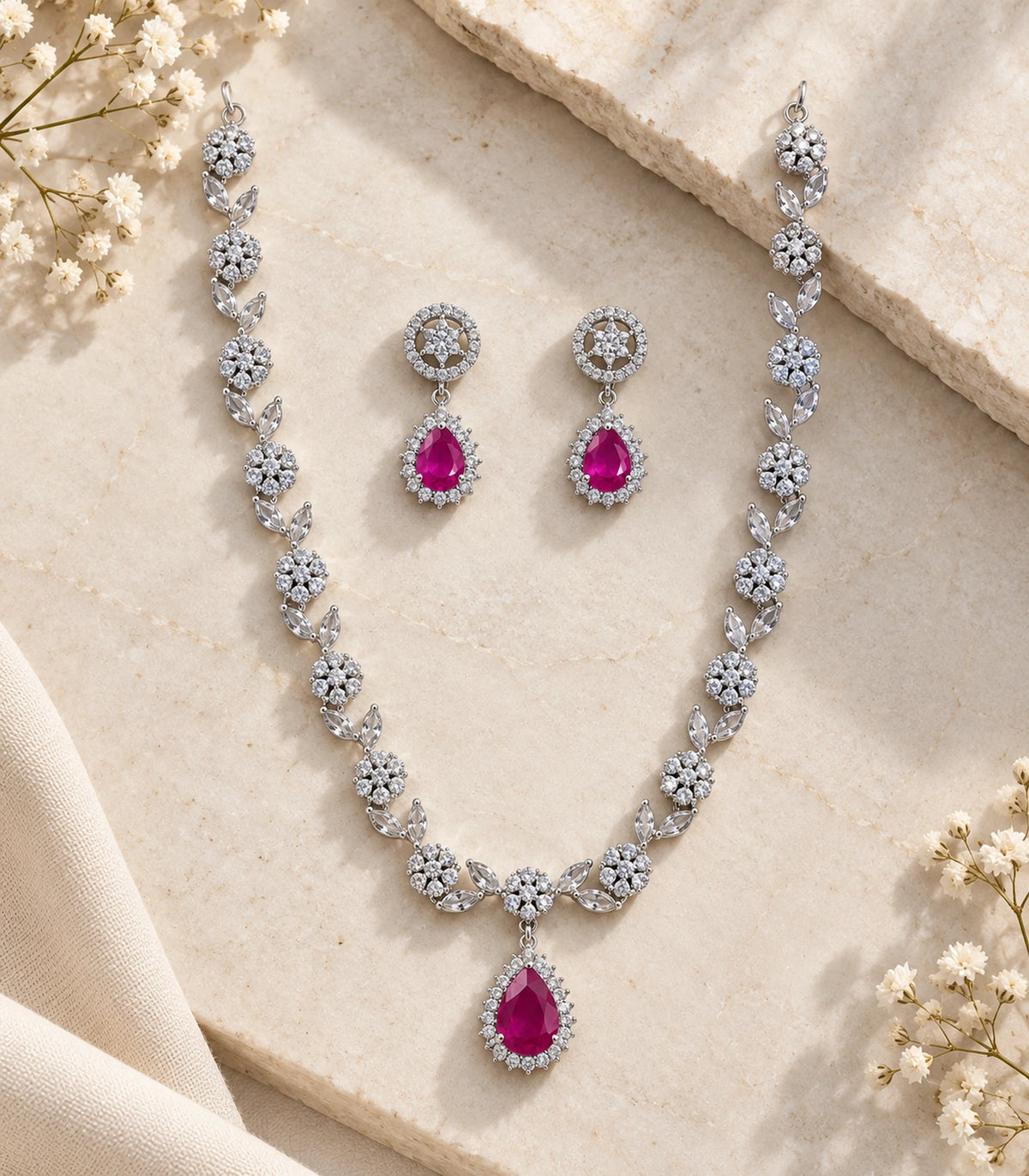 Complete silver-tone necklace and matching magenta teardrop earrings arranged on a stone surface