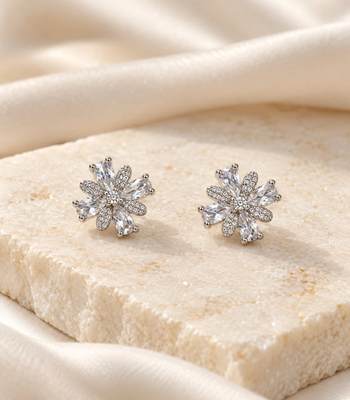 Matching silver-tone floral stud earrings displayed on a cream stone surface