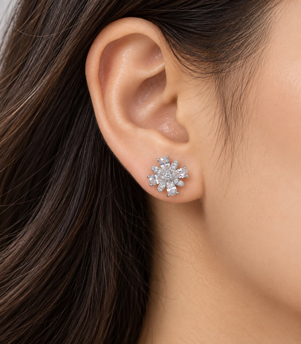 Silver-tone floral stud earring worn on an ear, showing clear faceted accents and alternating pavé-style petals