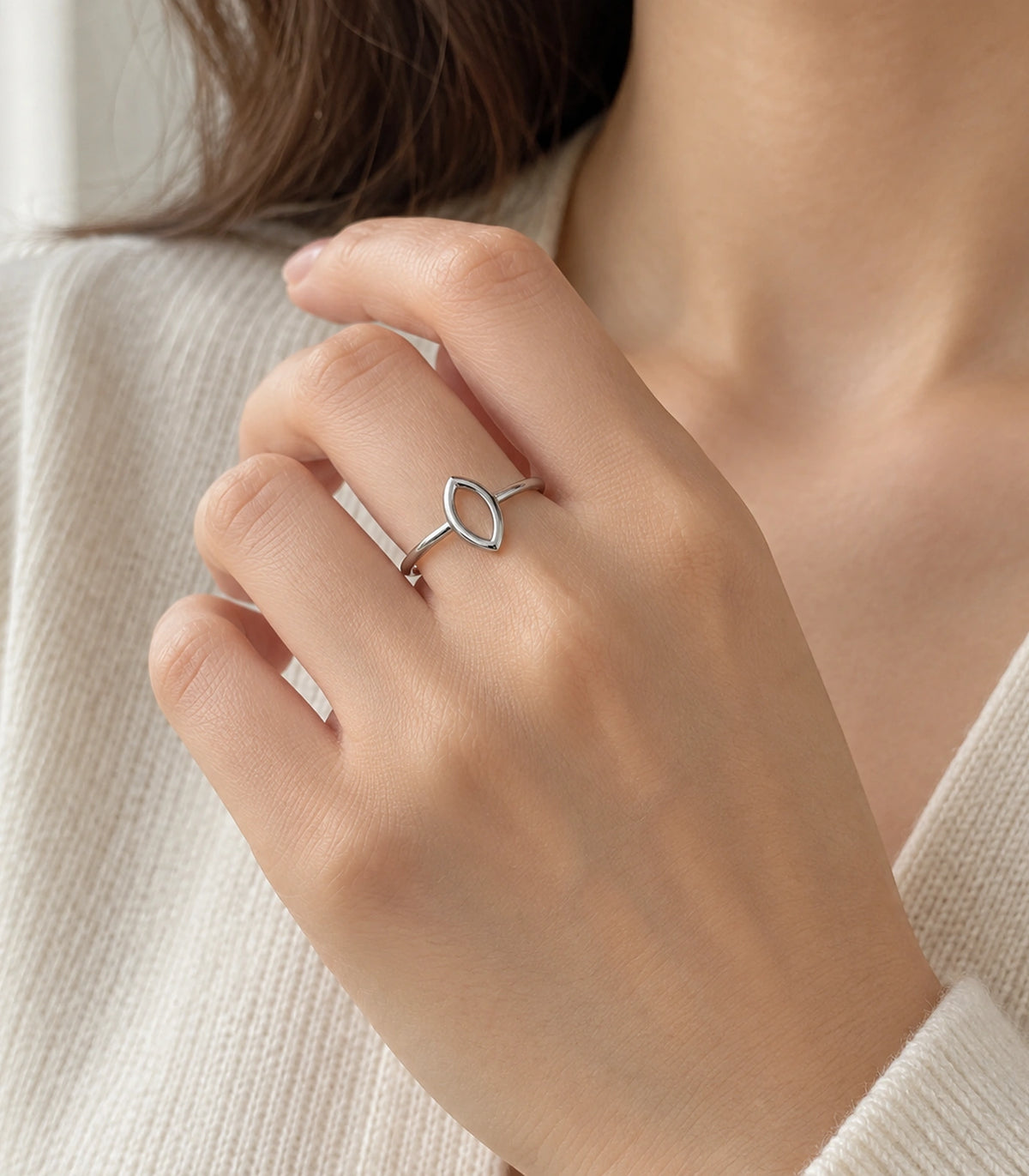 Silver-tone marquise ring worn on a hand near a cream knit neckline
