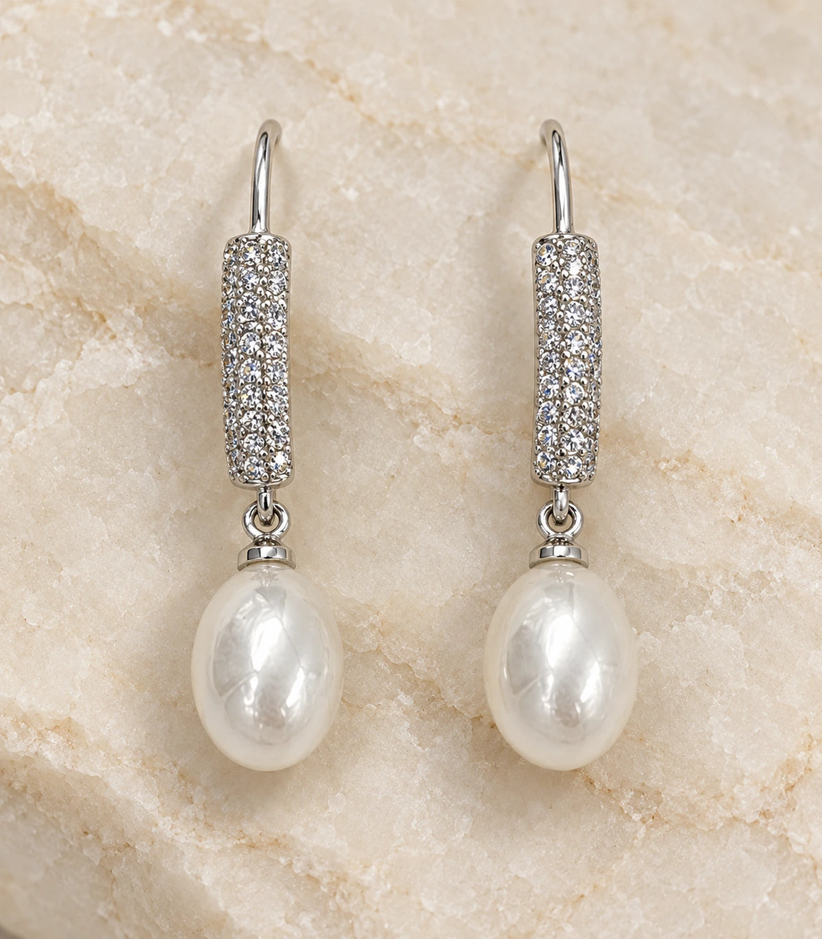 Detailed view of the matching pavé bar and white teardrop pearl-style earring pair on pale stone