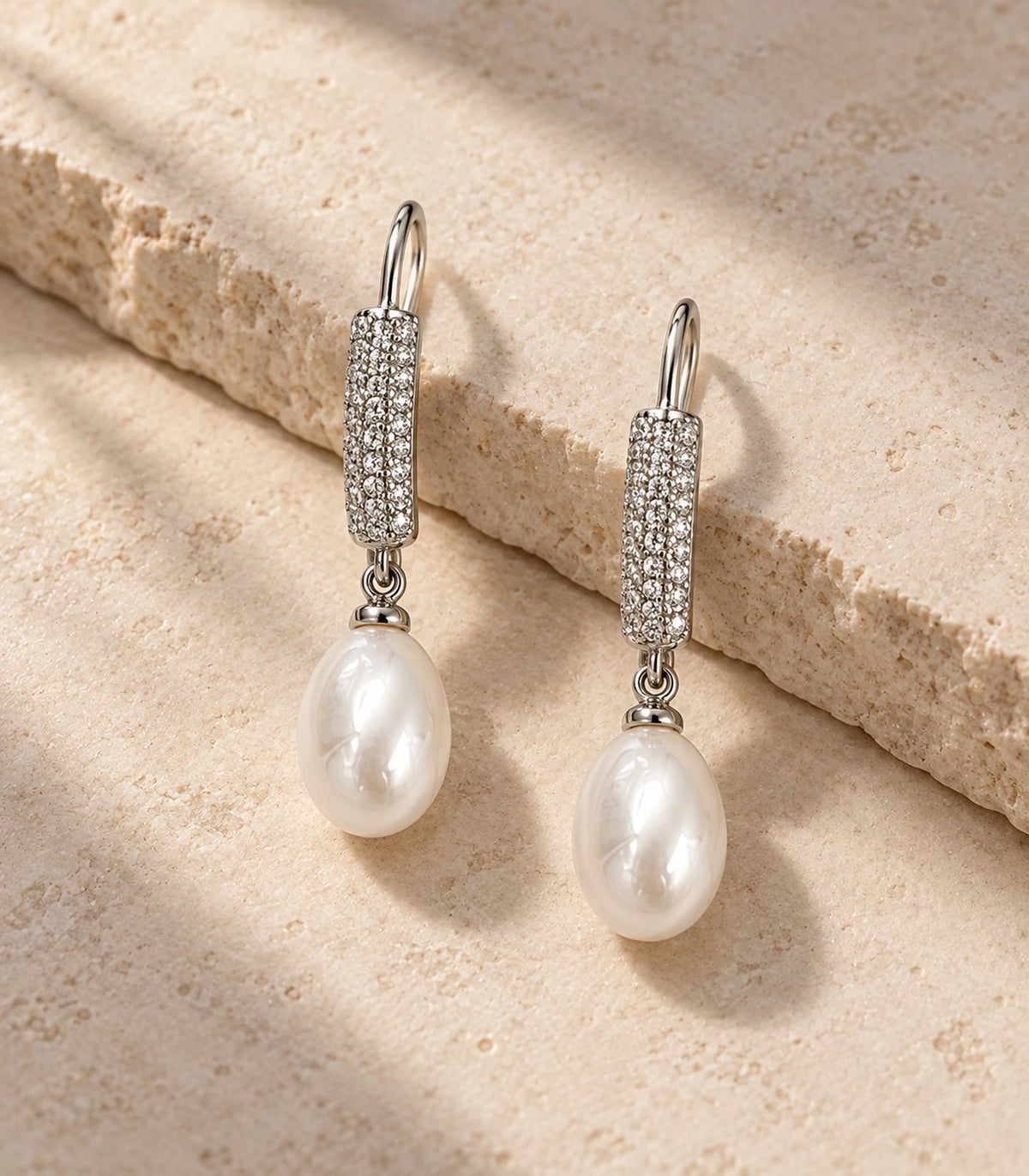 Matching silver-tone pavé bar and white teardrop pearl-style earrings arranged on stone