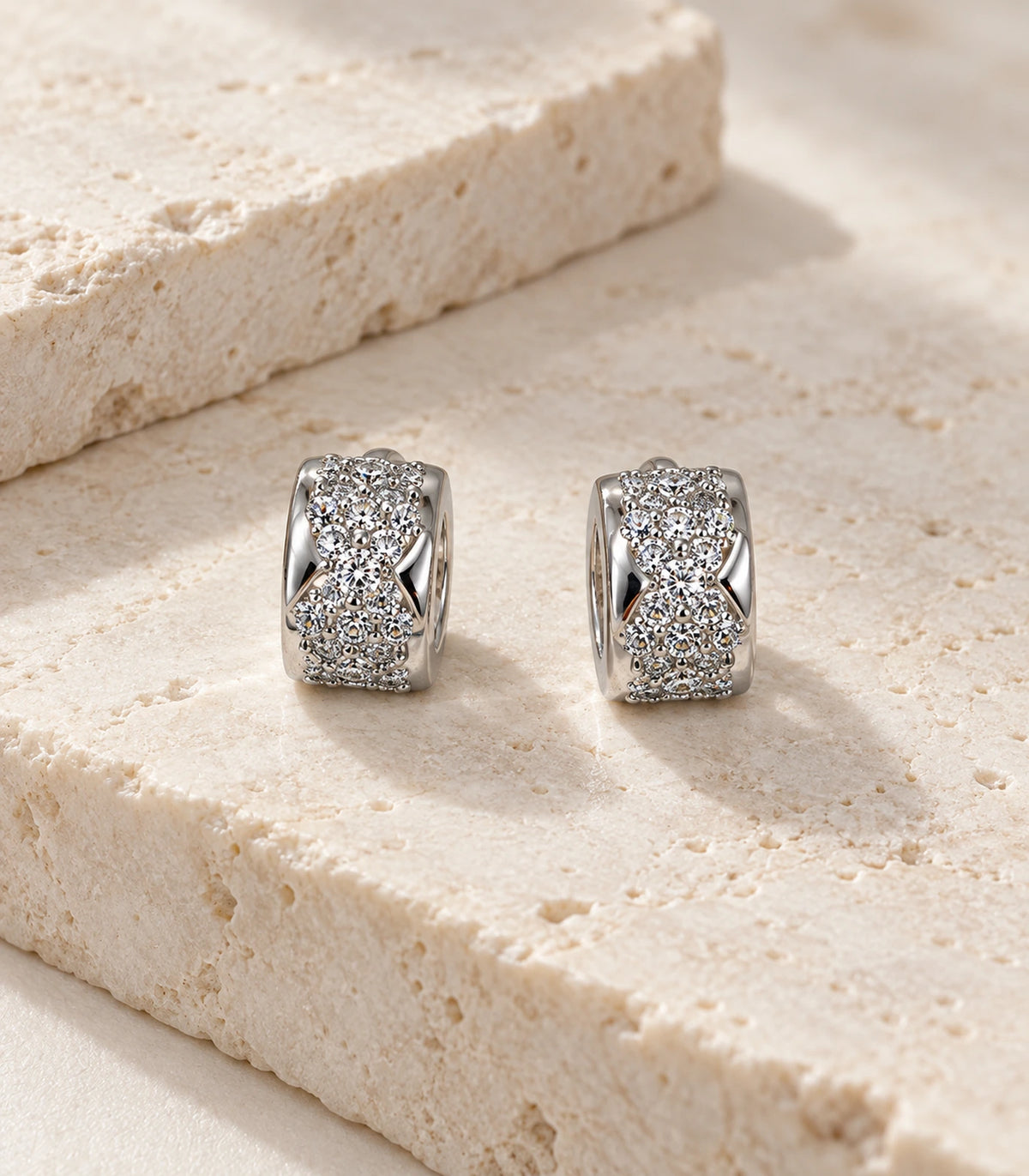 JIMIKI Silver Pave Bow Cross Huggie Earrings — editorial flat lay #color_silver