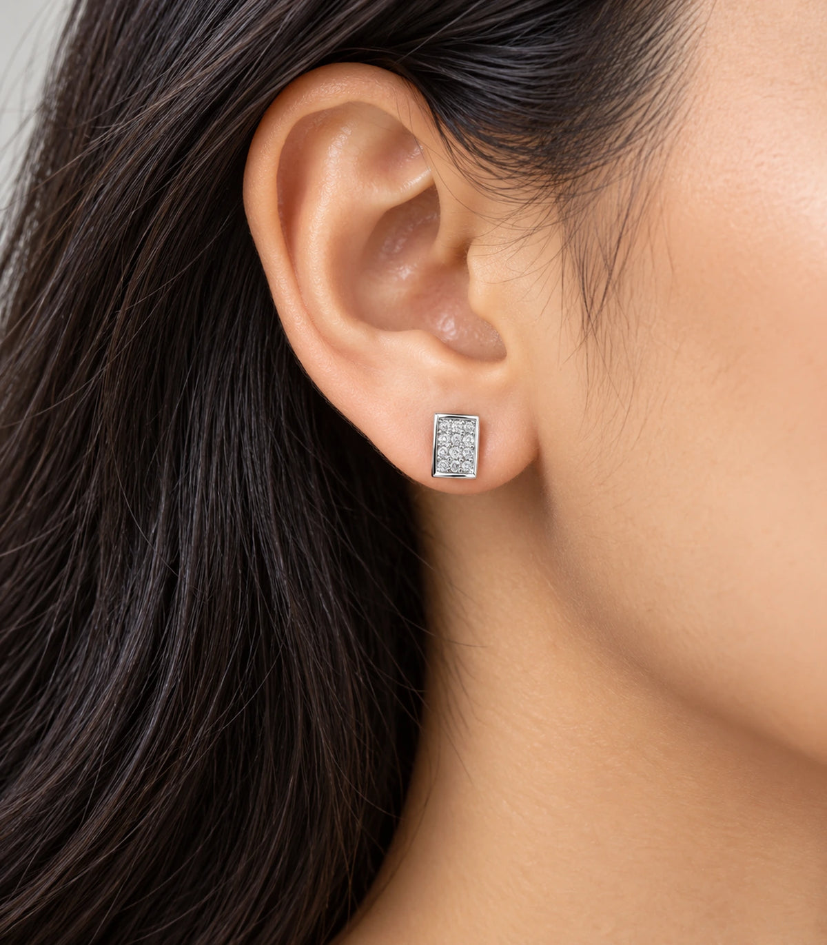Silver-tone rectangular pavé stud earring worn on the ear in an editorial side view