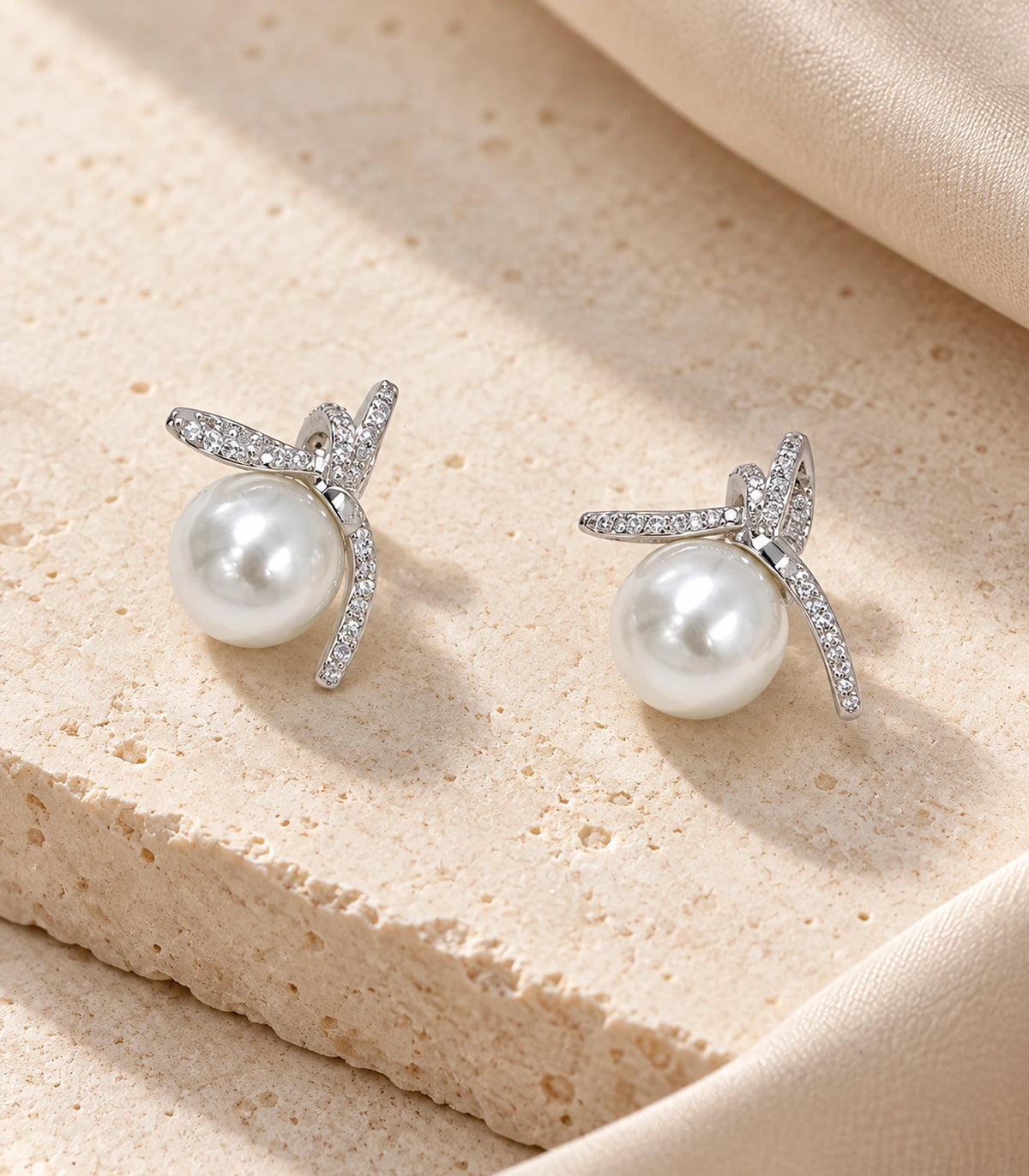 Pair of silver-tone pavé star pearl-look stud earrings arranged on warm stone