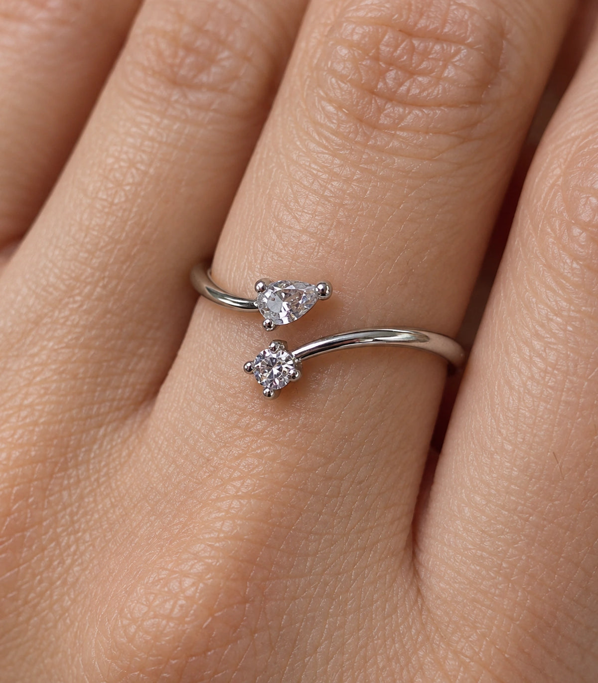 Closeup of the pear three-prong and round four-prong crystal settings on a worn silver-tone bypass ring