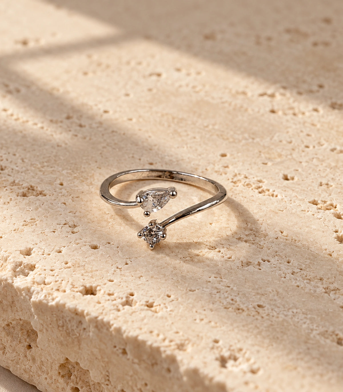 Complete silver-tone pear and round crystal bypass ring on a textured stone surface