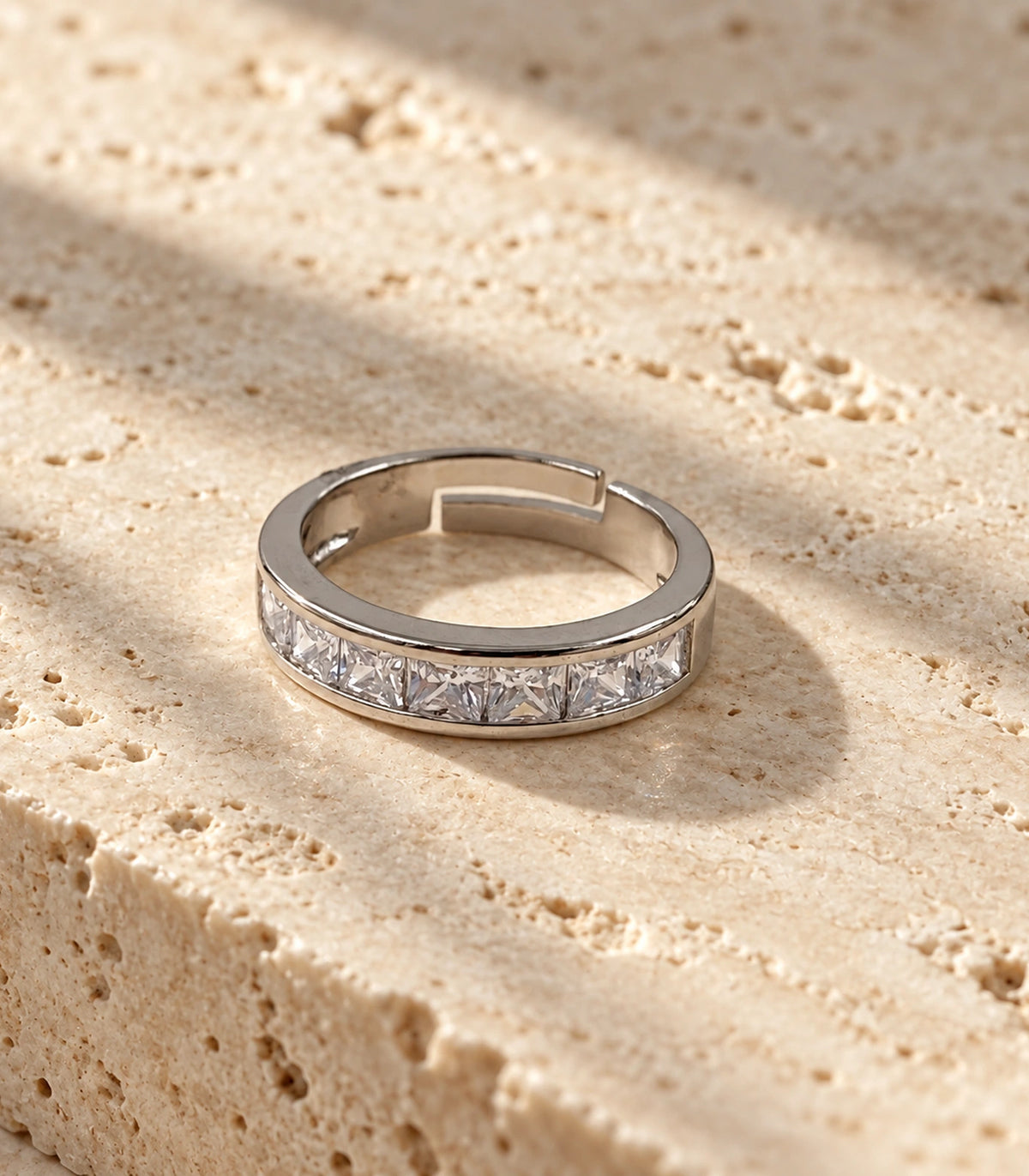 Complete silver-tone open channel band ring on a beige stone surface