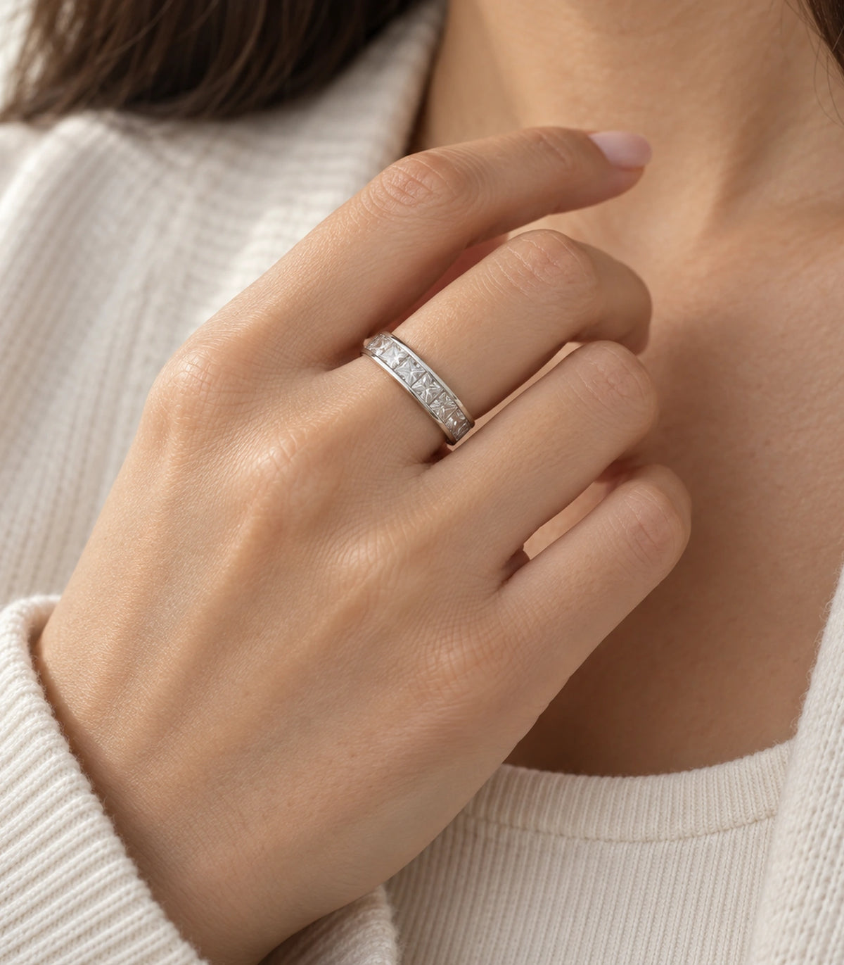 Silver crystal channel band ring worn with a hand beside a cream neckline