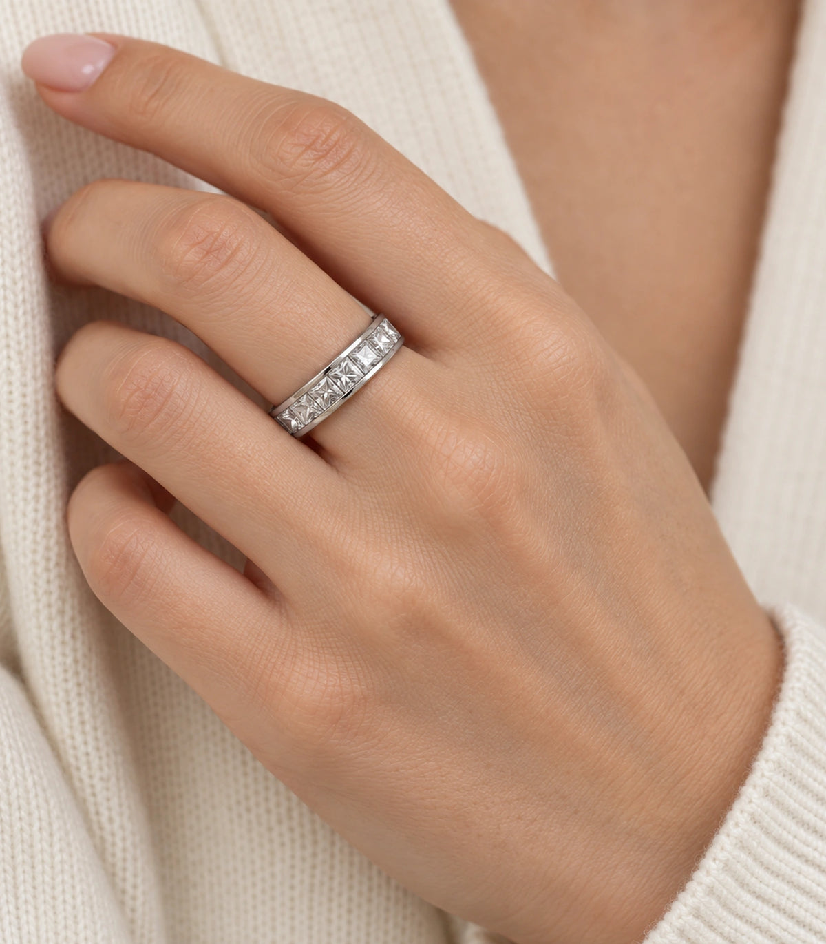 Silver square crystal channel band ring worn on a finger with cream knit styling
