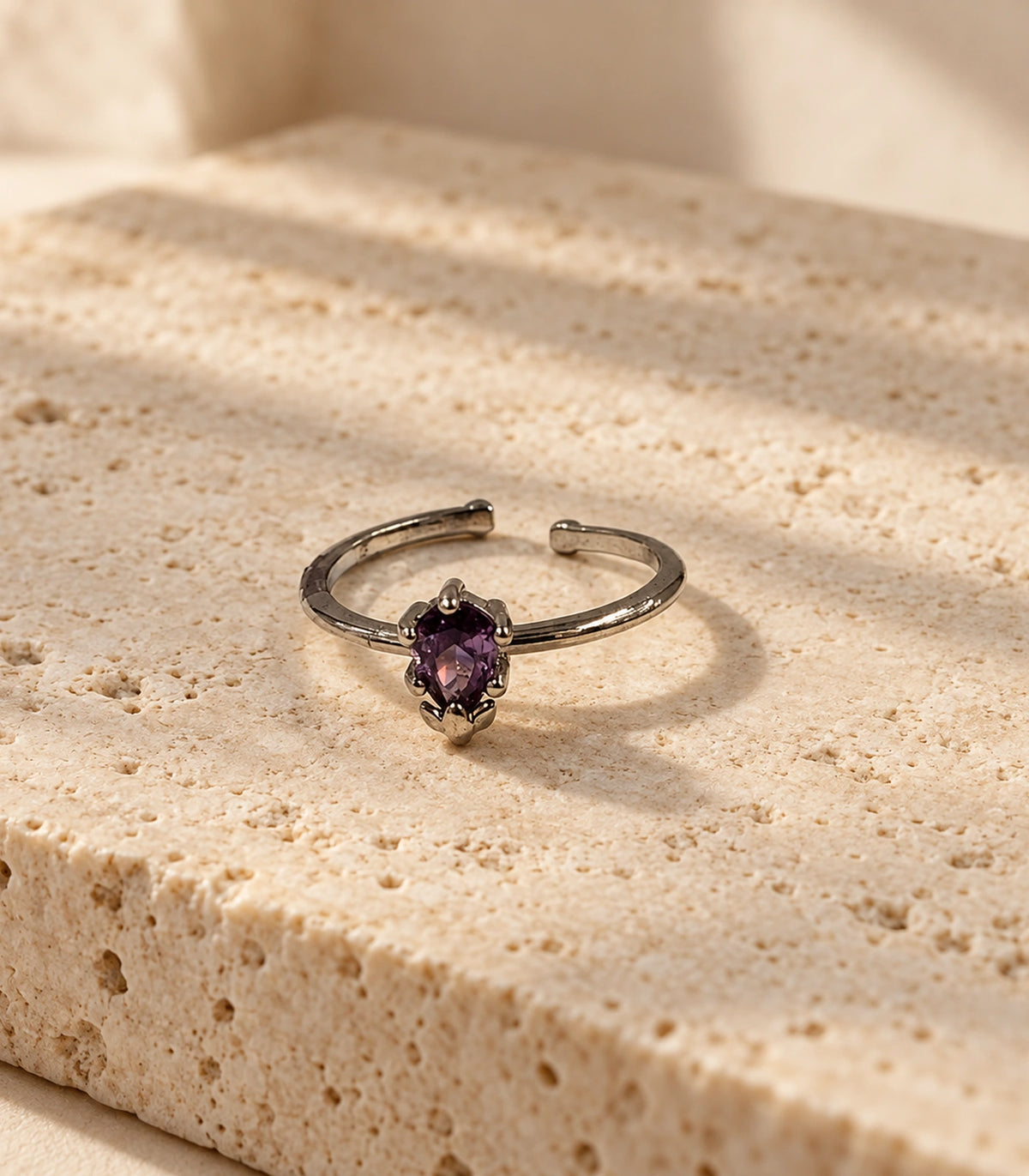 Complete silver-tone purple solitaire ring styled on a beige stone surface