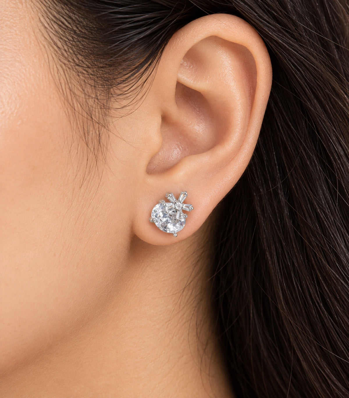 Silver-tone round clear crystal-style stud earring with baguette burst accents worn on an ear
