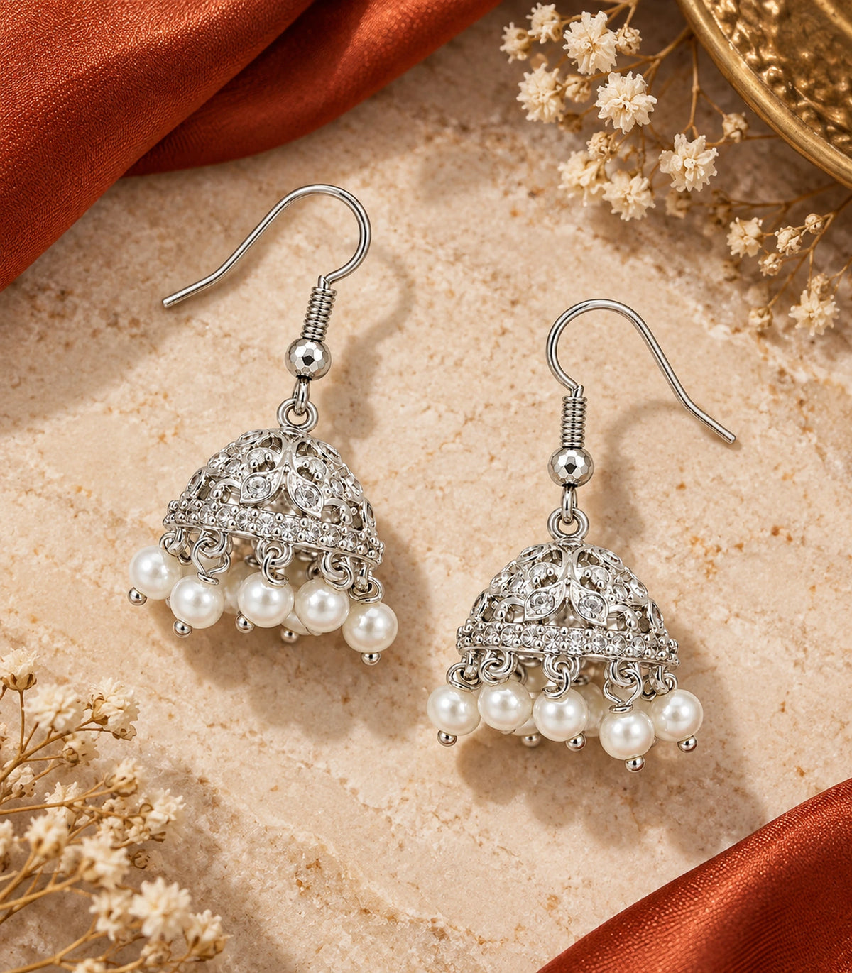 JIMIKI Silver Round Crystal Openwork Jhumka Earrings - Matching pair on pale stone beside rust fabric #color_silver