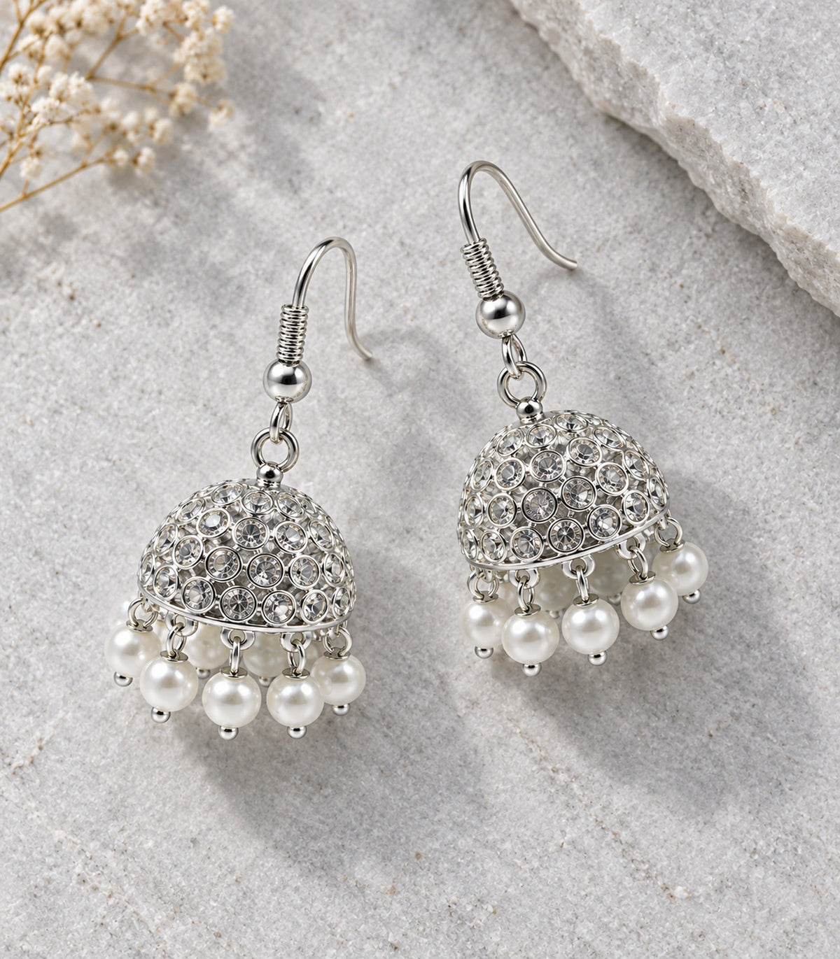 Silver-tone crystal-style jhumka pair with pearl-effect fringe arranged on pale stone #color_silver