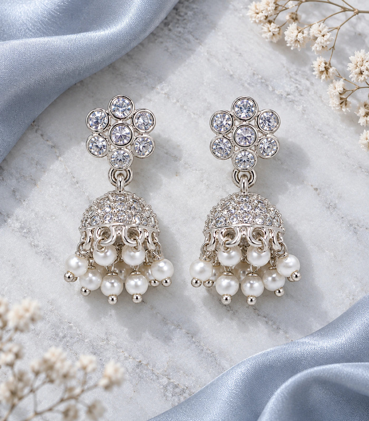 JIMIKI Silver Seven-Stone Flower Jhumka Earrings - Matching pair on a pale surface with blue fabric #color_silver