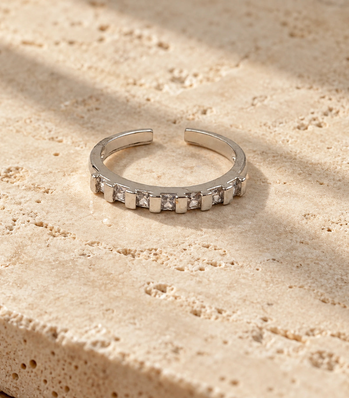 Complete silver-tone open-back crystal bar ring on a light stone surface