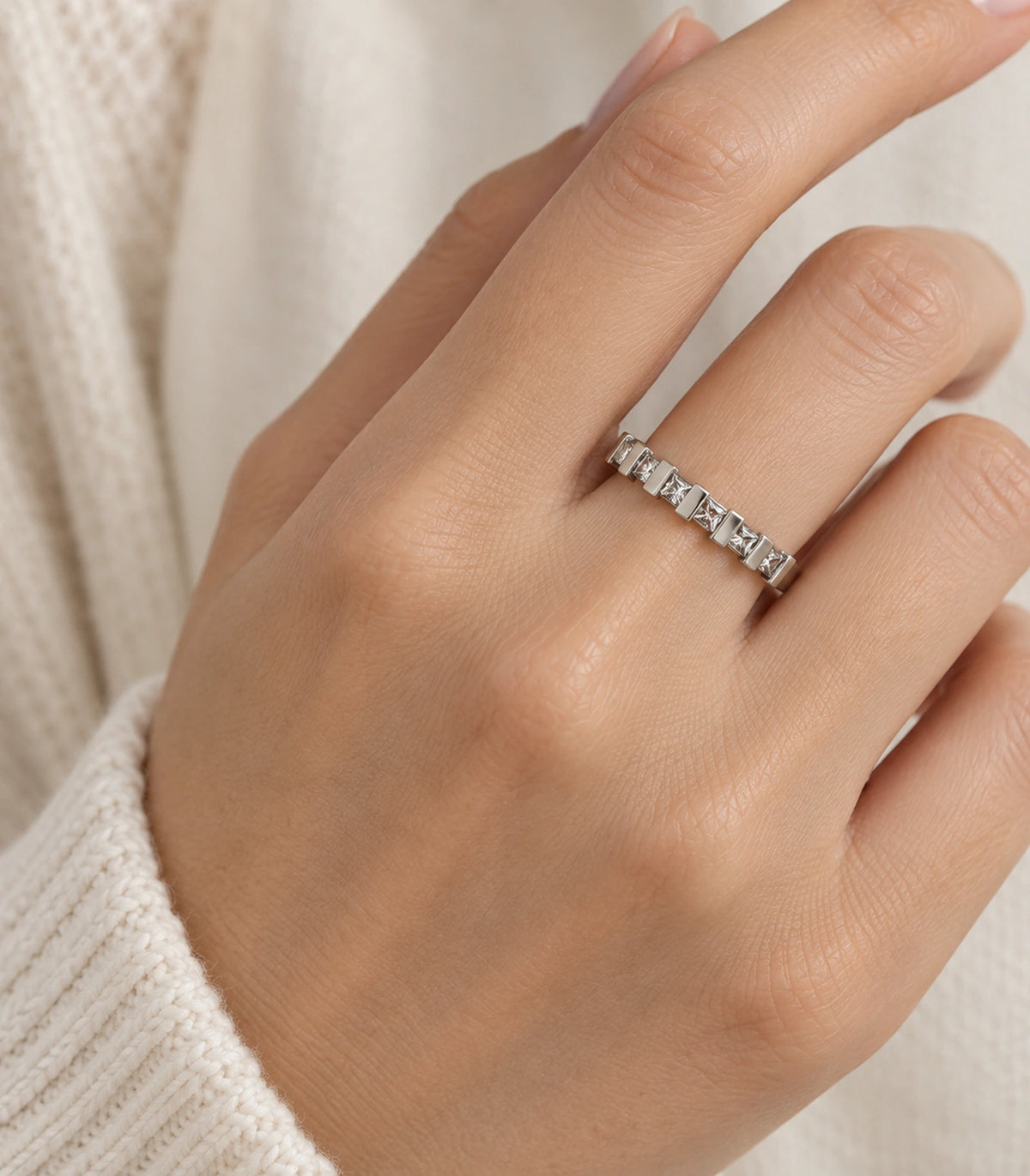 Silver square crystal bar pattern ring worn naturally on a finger with a cream sleeve