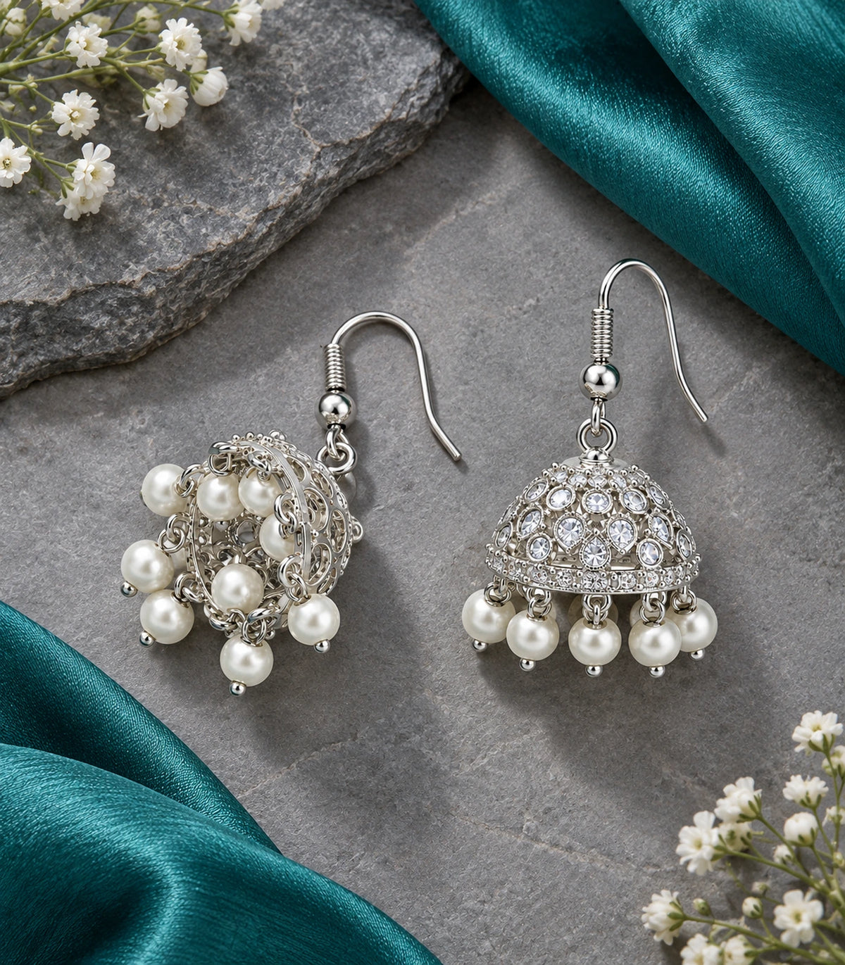 JIMIKI Silver Teardrop Crystal Openwork Jhumka Earrings - Matching pair on grey stone beside teal fabric #color_silver