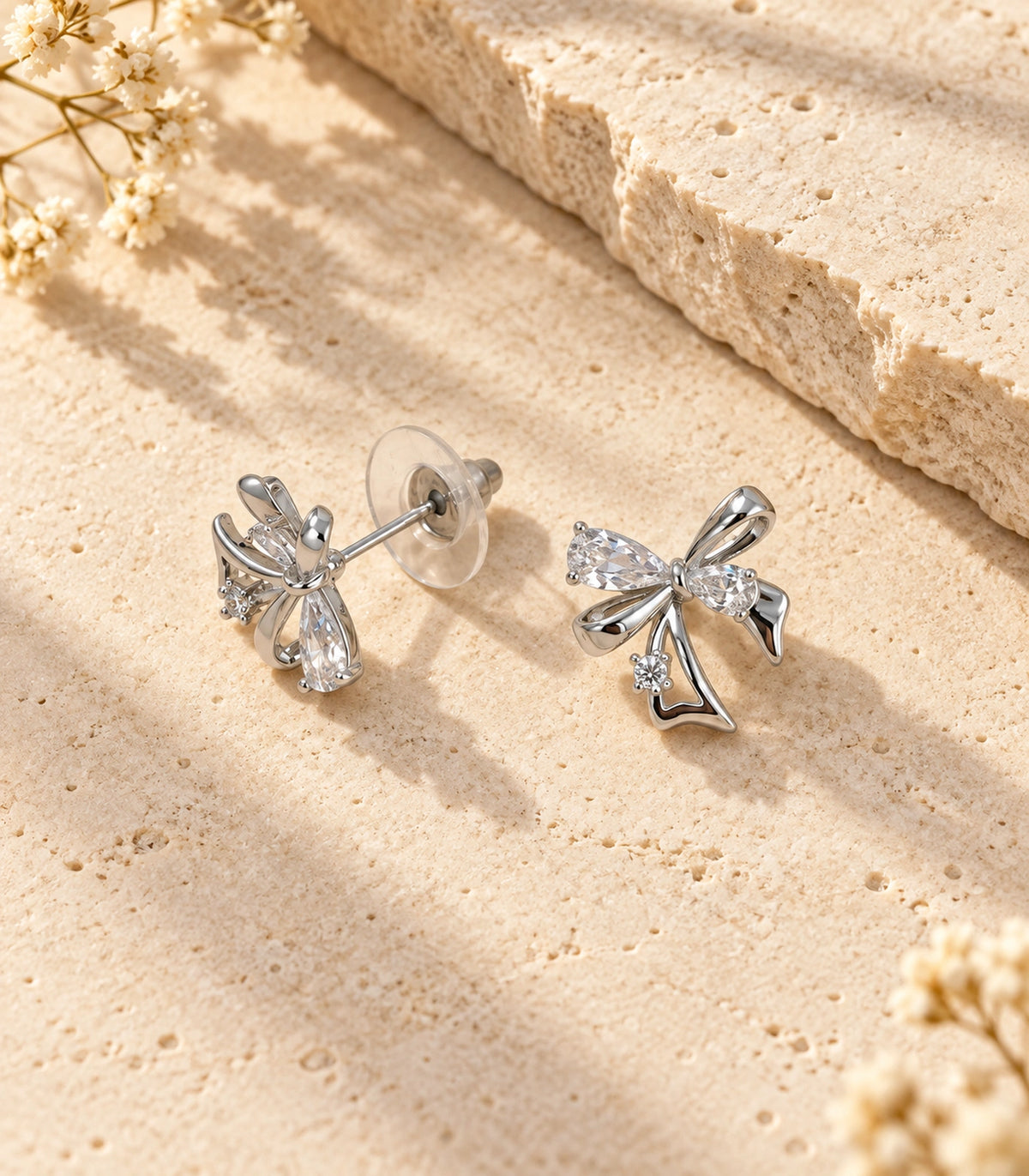 JIMIKI Asymmetric Crystal Bow Stud Earring Pair in Silver / Clear, editorial flat lay #color_silver / clear