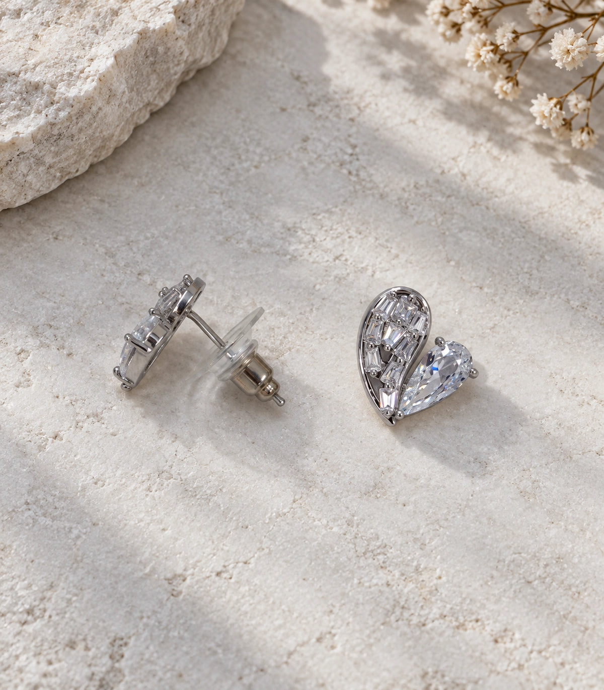 JIMIKI Asymmetric Crystal Heart Stud Earring Pair in Silver Tone, editorial flat lay #color_silver tone