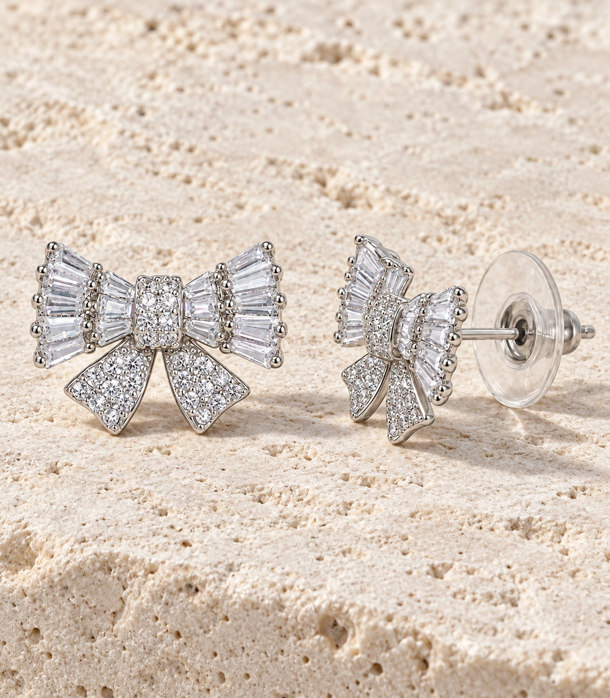 JIMIKI Baguette Crystal Bow Stud Earring Pair in Silver-tone, editorial flat lay #color_silver-tone