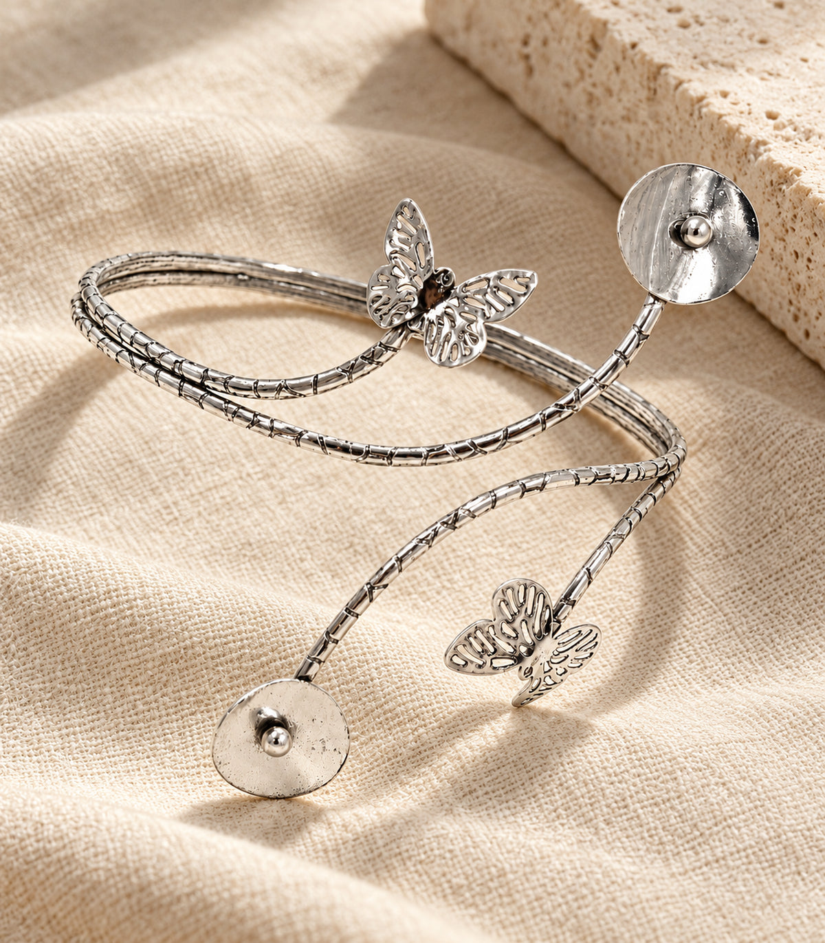 Complete silver-tone butterfly disc arm cuff arranged on linen and stone