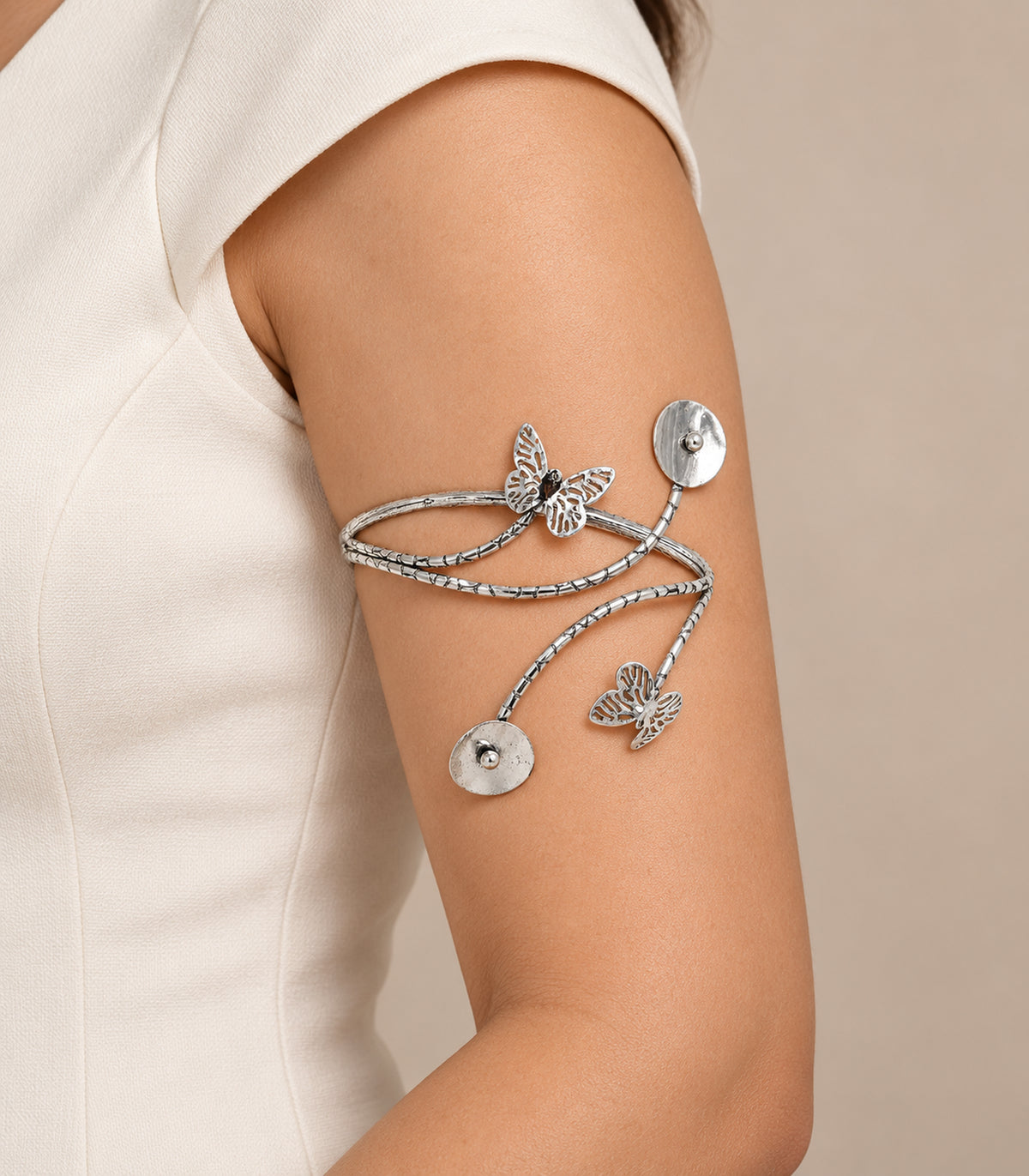 Silver-tone butterfly and disc cuff worn on the upper arm with ivory clothing