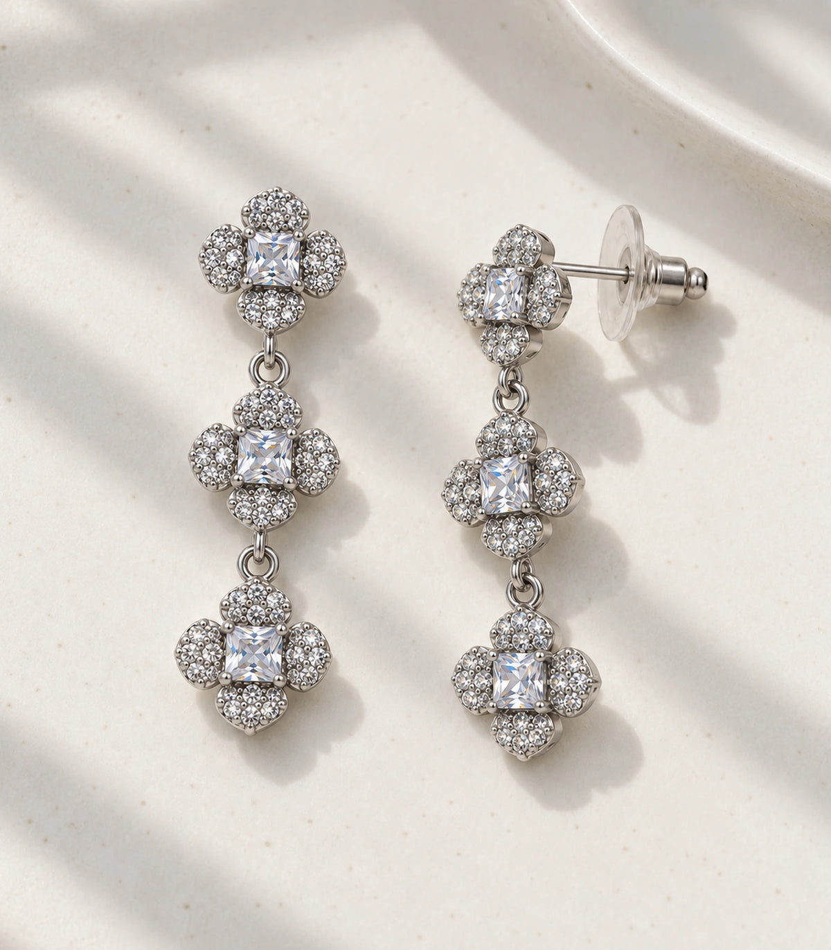 JIMIKI Triple Four Petal Flower Drop Earring Pair in Silver tone / clear, editorial flat lay #color_silver tone / clear