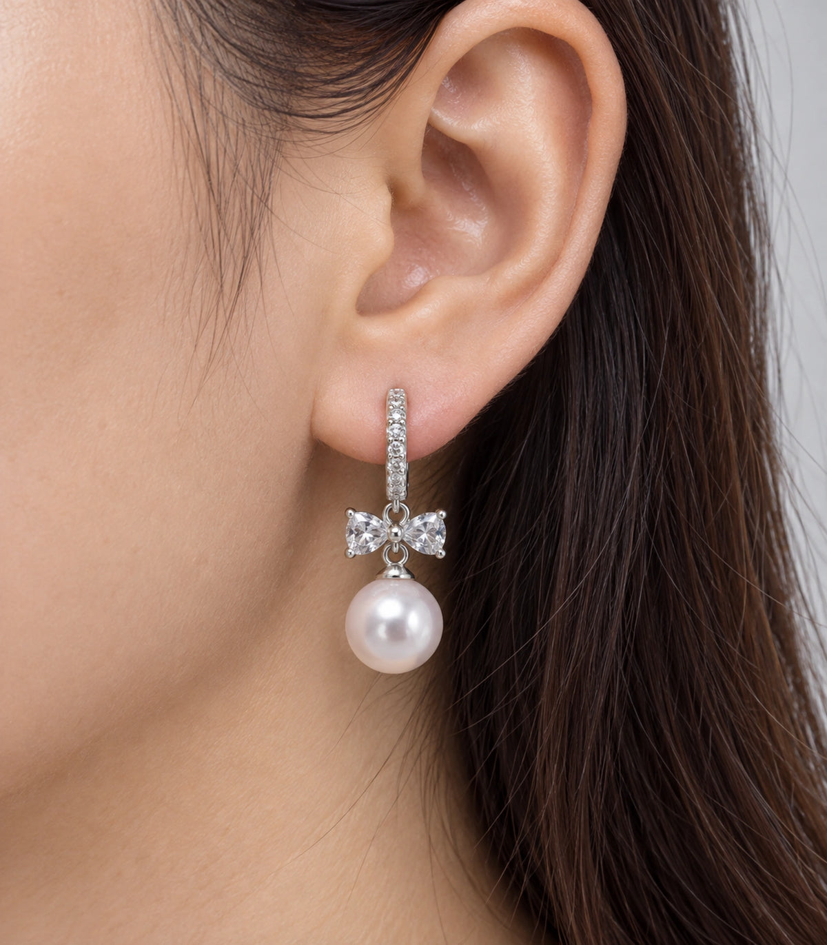 JIMIKI Silver-Tone Crystal Bow Pearl-Drop Huggie Earrings in Silver / Clear / White, close-up detail