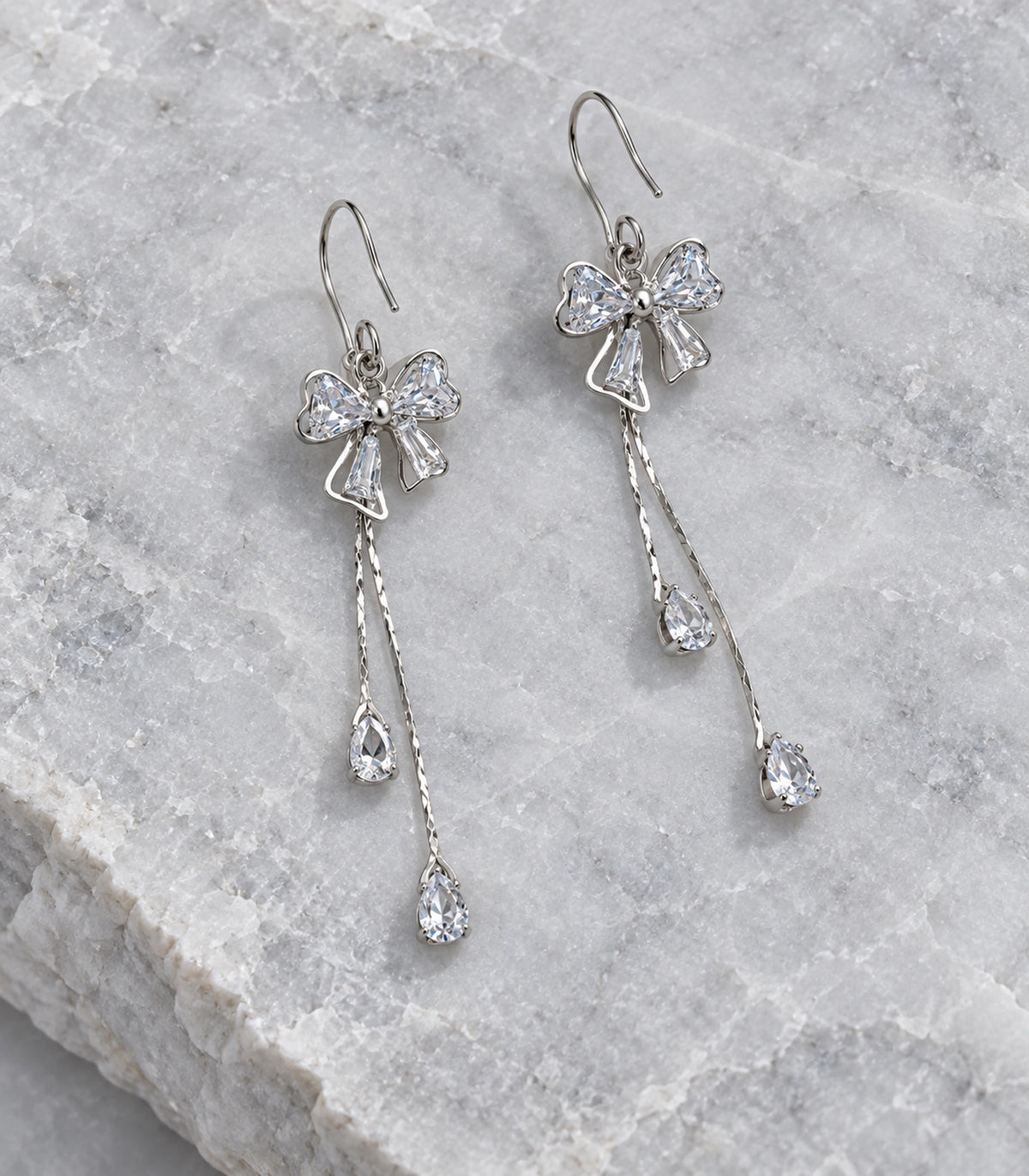 JIMIKI Silver-Tone Crystal Bow Twin Pear Drop Earrings in Silver Tone, editorial flat lay