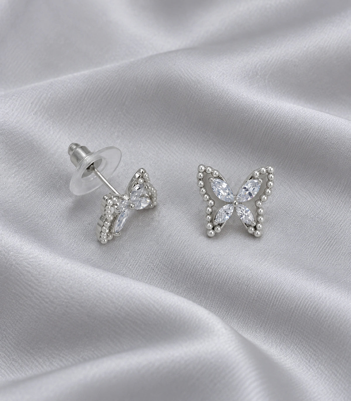 JIMIKI Silver-Tone Crystal Butterfly Stud Earrings in Silver / Clear, editorial flat lay