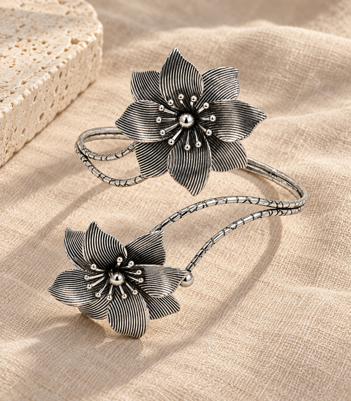 Complete silver-tone double-flower arm cuff arranged on linen and stone
