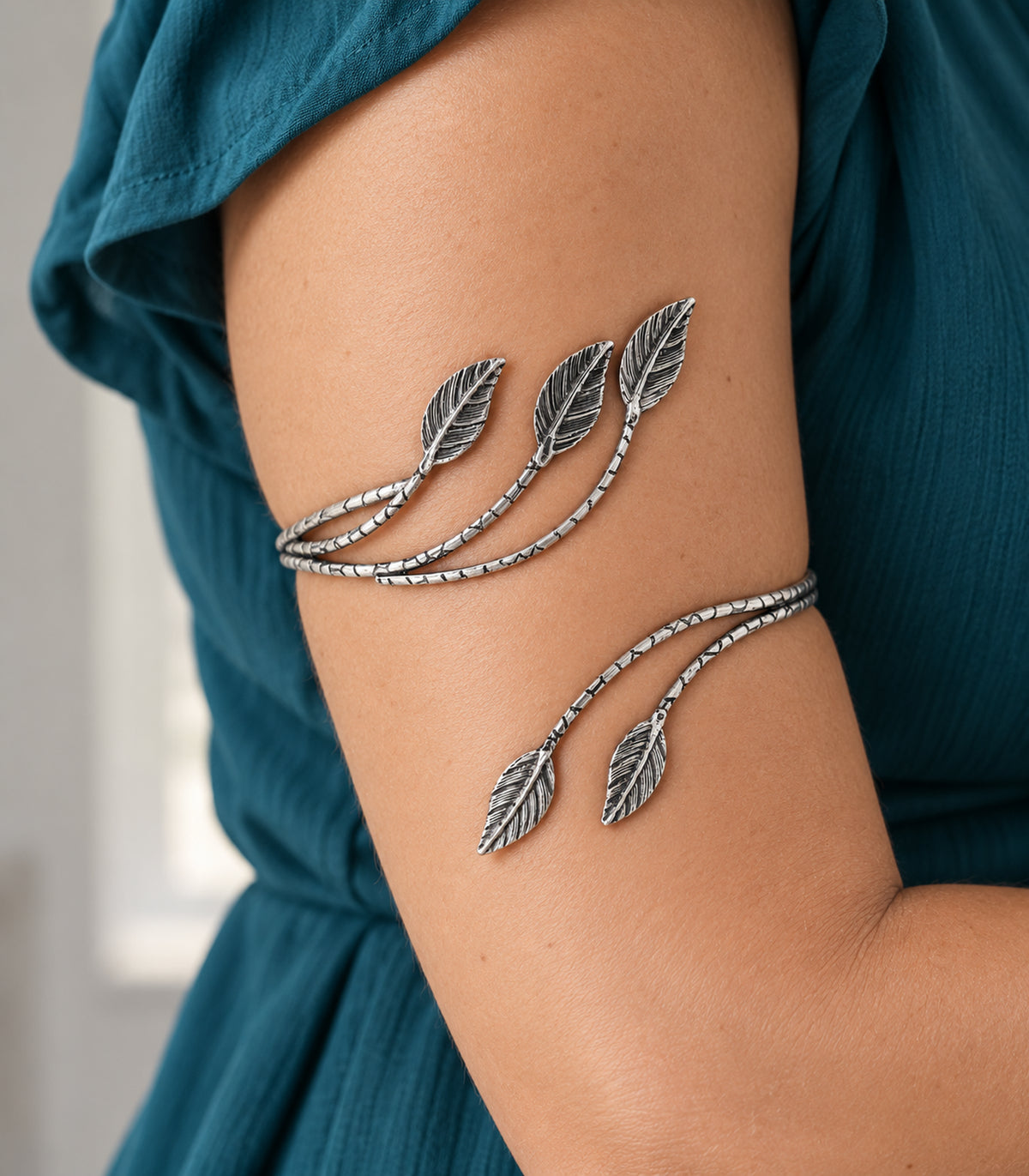 Close view of five engraved leaves and textured silver-tone branches worn on upper arm